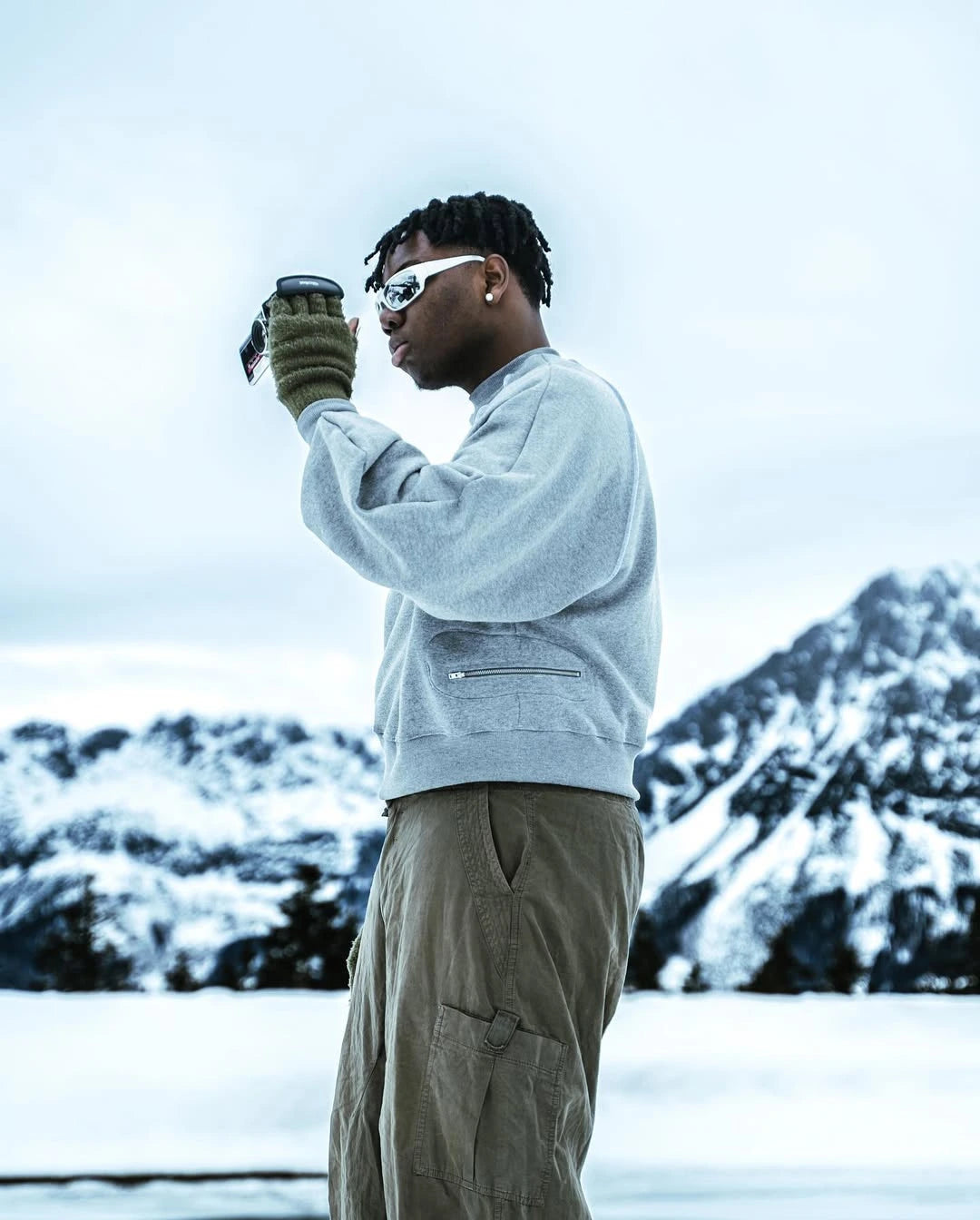 Person in a snowy landscape wearing a light gray sweatshirt and beige pants.