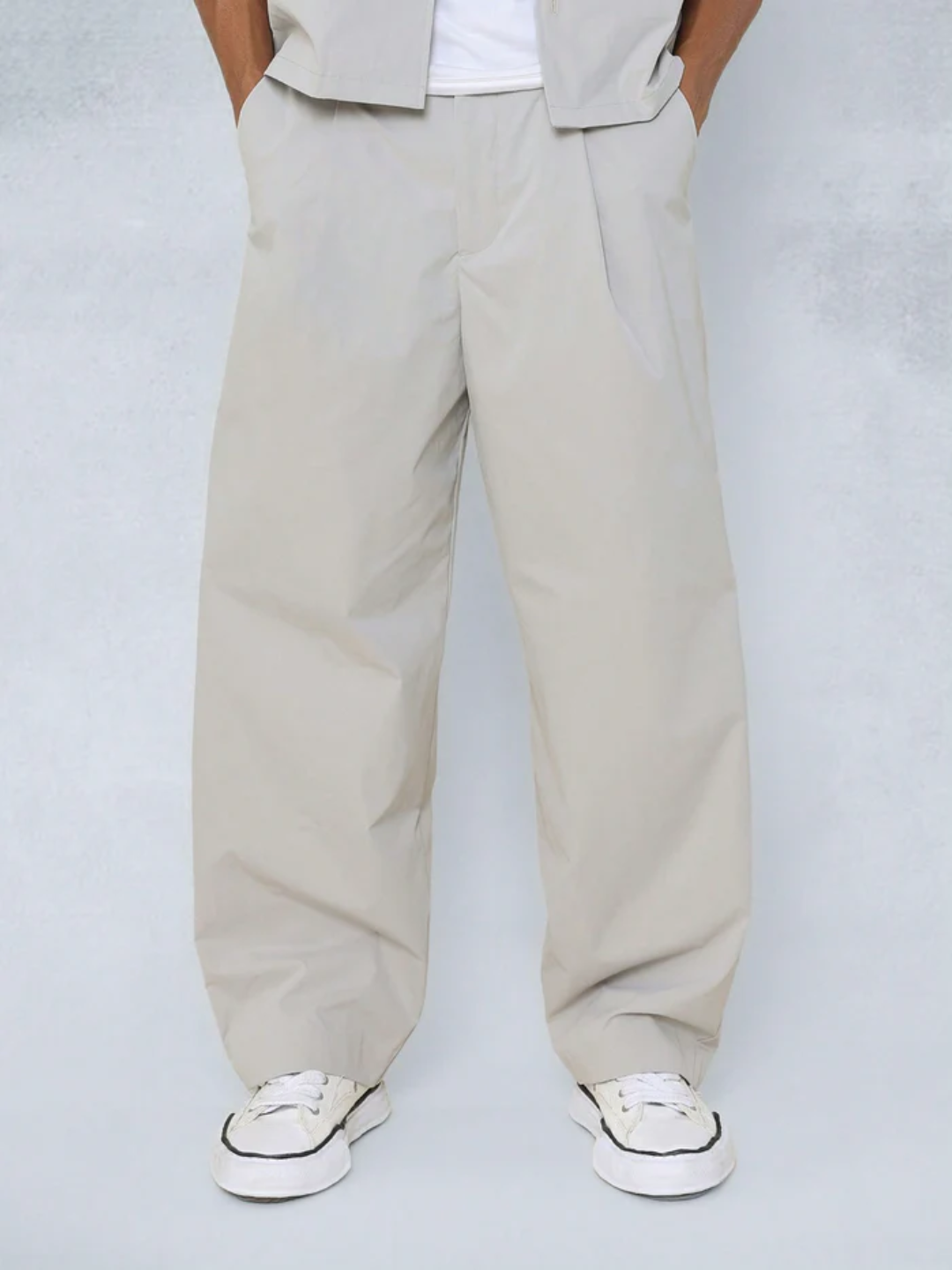 A male model wearing a Grey crop fit shirt with a classic collar and drop shoulder sleeves, paired with beige loose fit pants.