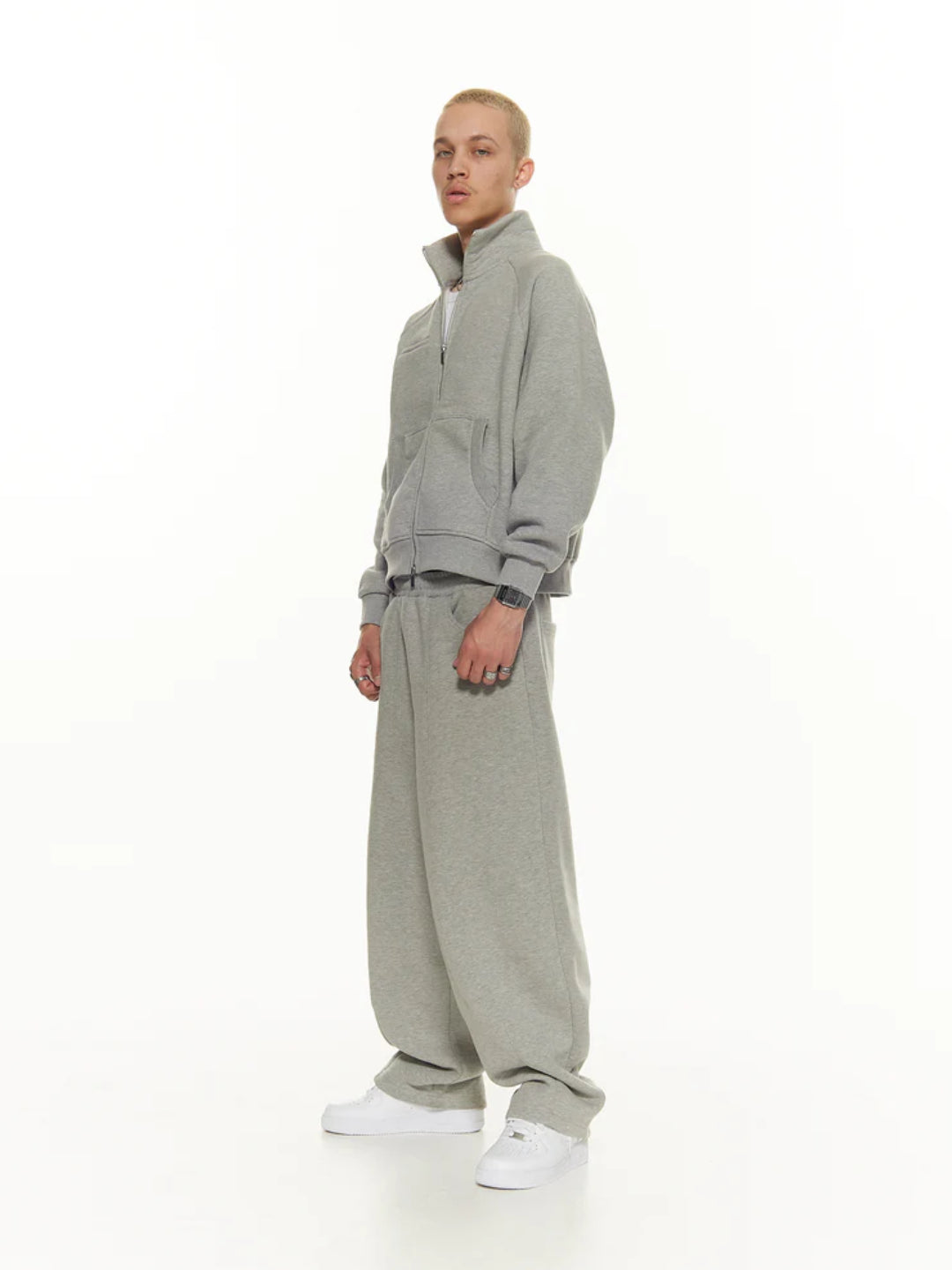 A male model wearing a Grey track jacket with double zippers and a white graphic on the sleeve, standing against a white background.