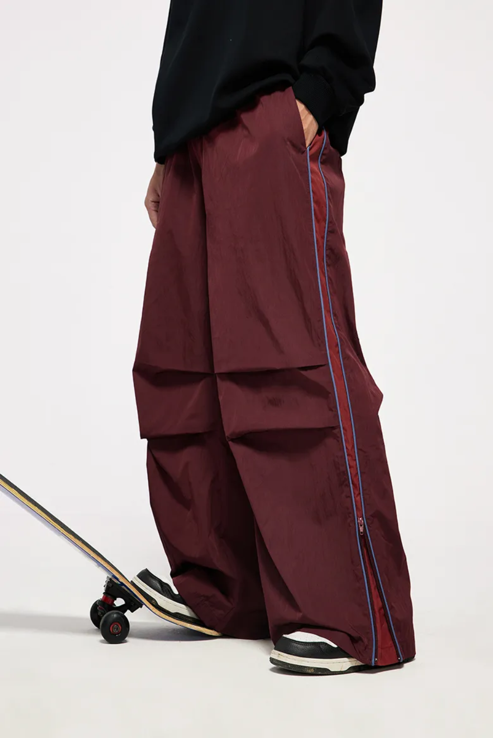 A person wearing vintage sporty pants in red-brown color, standing next to a skateboard.