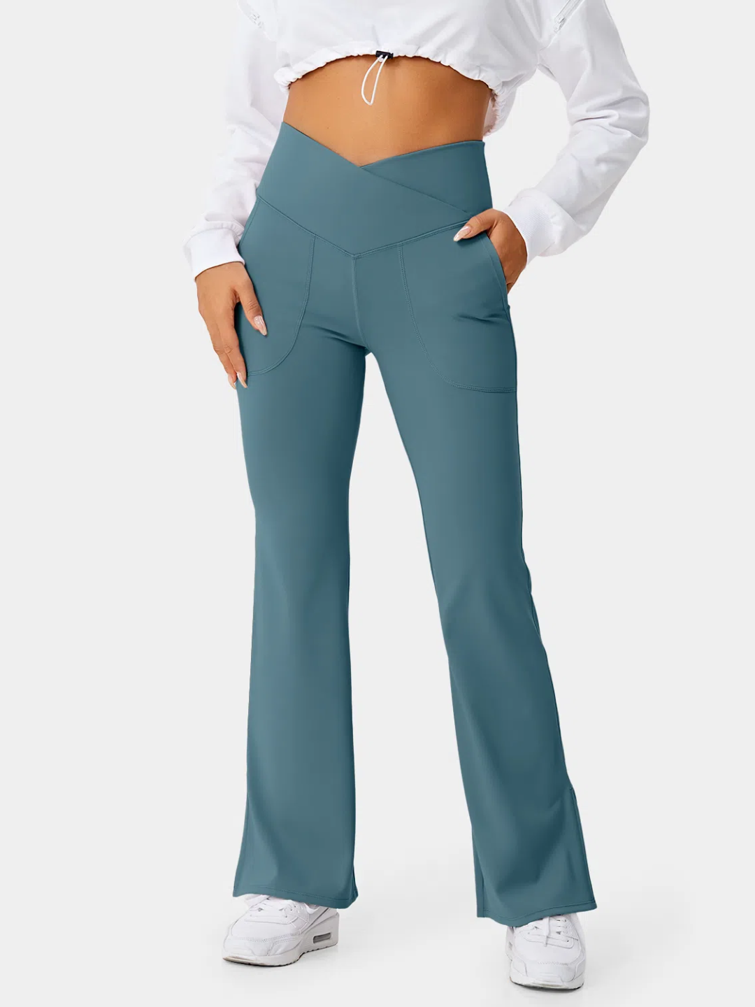 A person wearing teal flare leggings with a split hem, paired with a white cropped top and white sneakers.