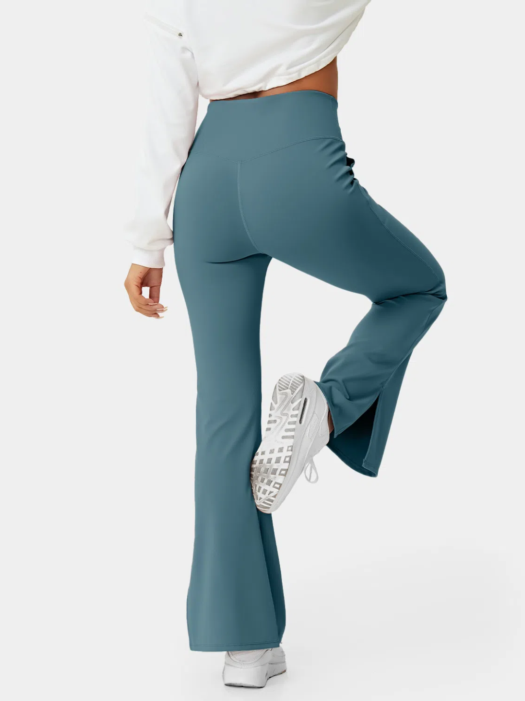 A person wearing teal flare leggings with a split hem, paired with a white cropped top and white sneakers.