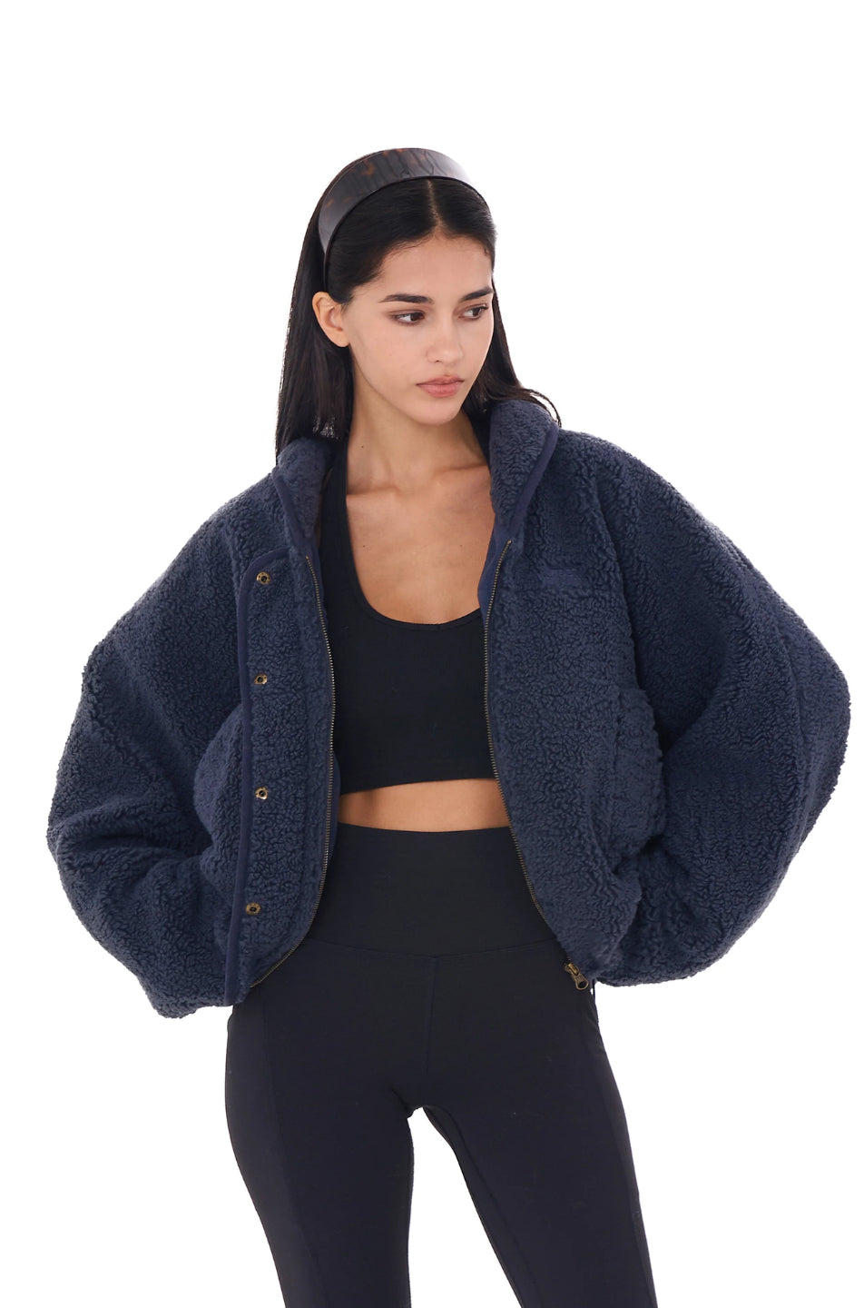 A woman wearing a navy blue fleece zip jacket with a full-zip front, paired with black leggings. The jacket is double-sided with one side smooth and the other textured fleece.