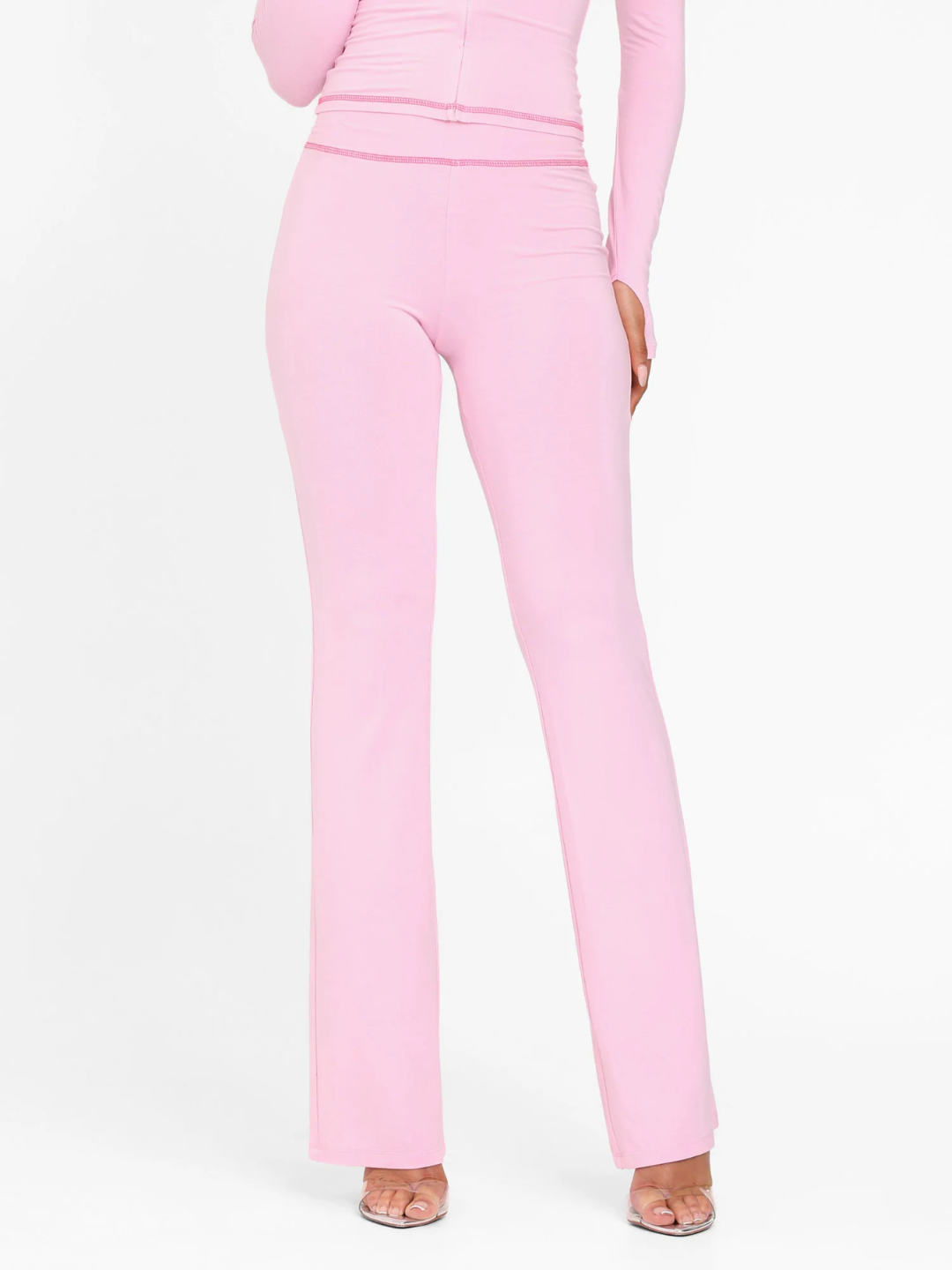 A female model wearing a pink long-sleeve hoodie and matching low-rise track pants with cherry placement prints and contrast stitching.