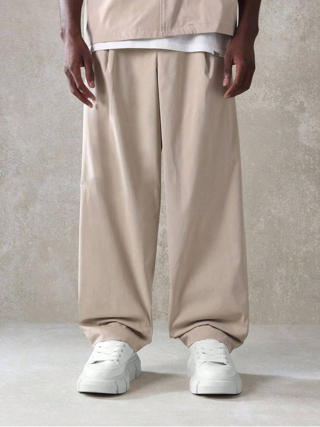 A male model wearing a Beige crop fit shirt with a classic collar and drop shoulder sleeves, paired with beige loose fit pants.