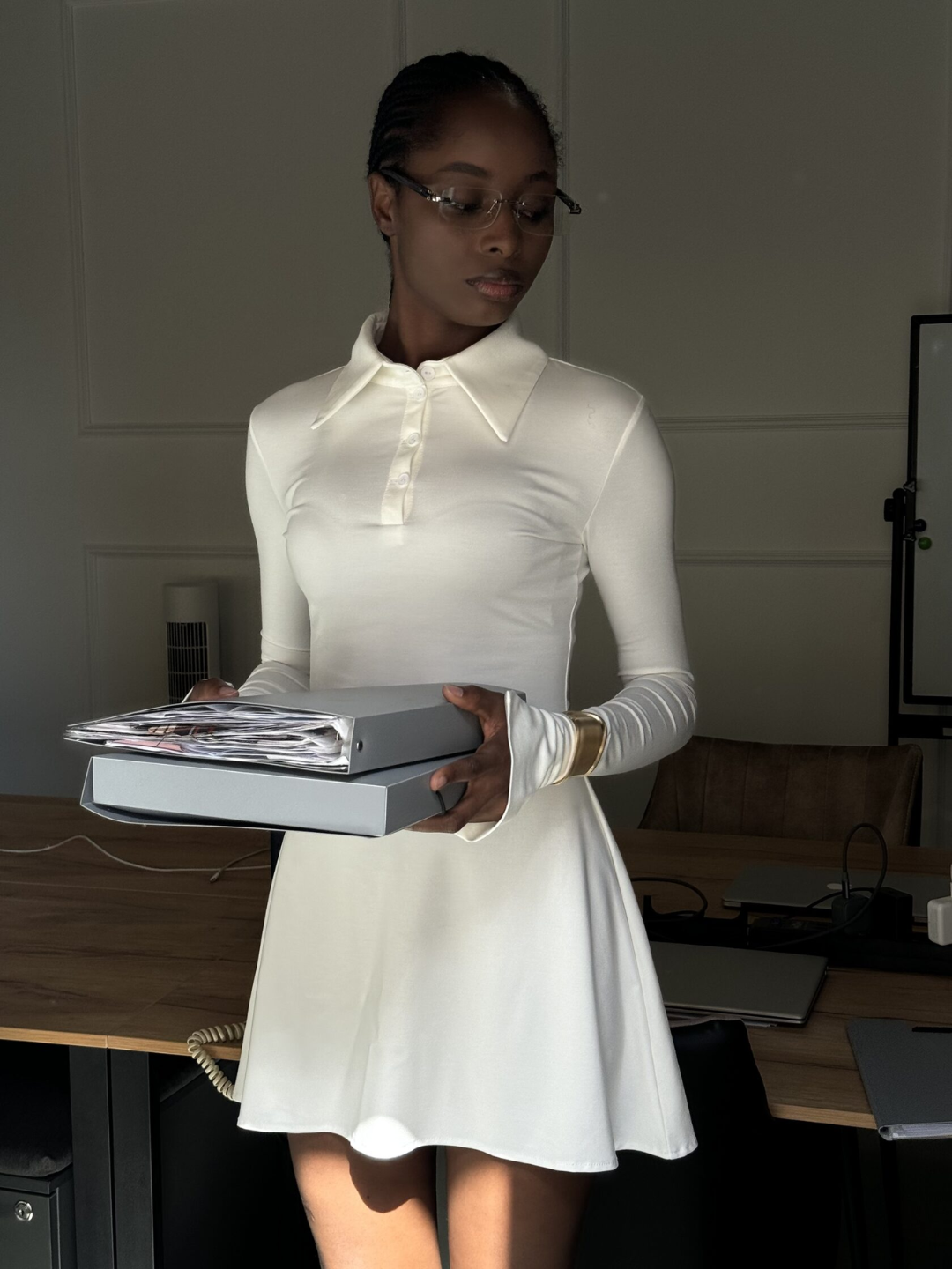 A person holding a stack of books wearing a white business dress with long sleeves, knee-length, and a collar.