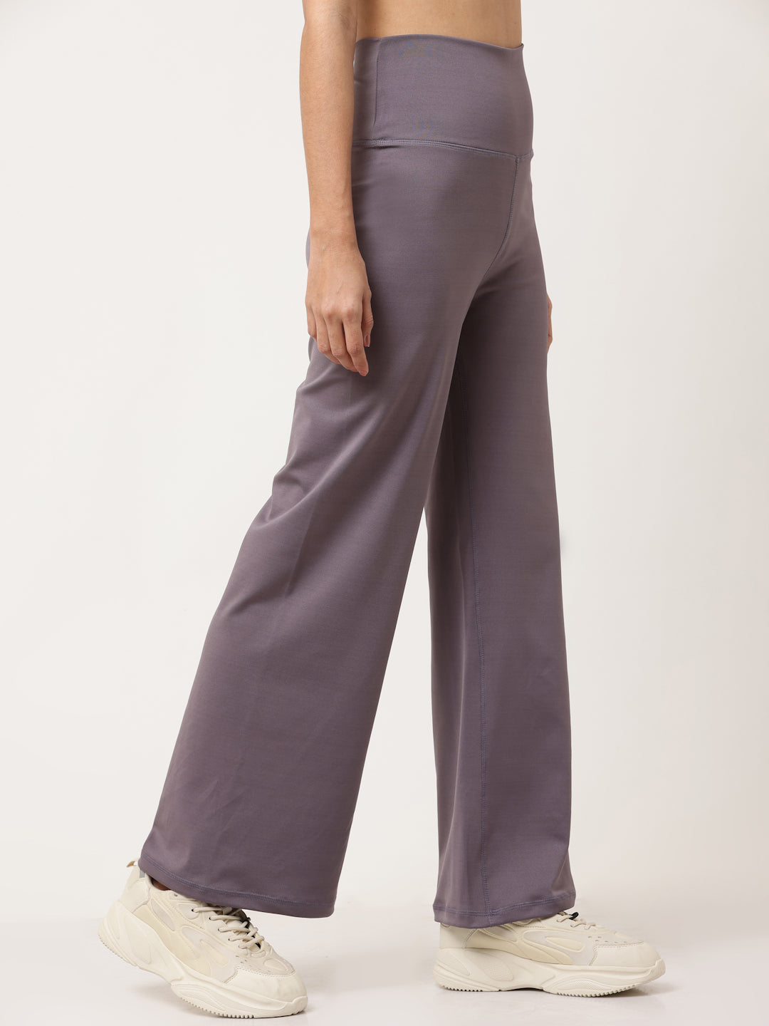 A woman standing and posing in lavender high-waisted full-length yoga pants with a solid black sports top.