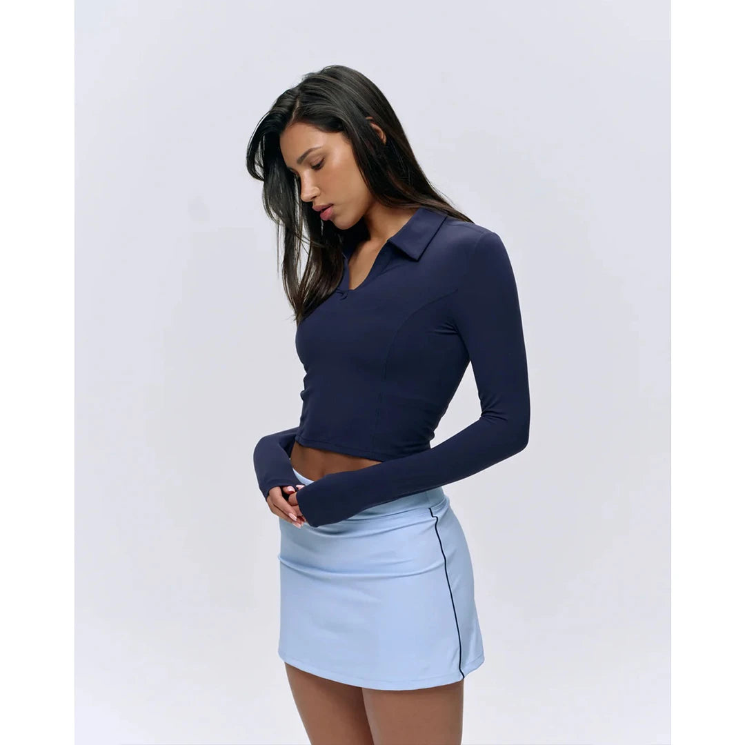 Woman wearing a navy long-sleeve top and light blue skirt on a white background