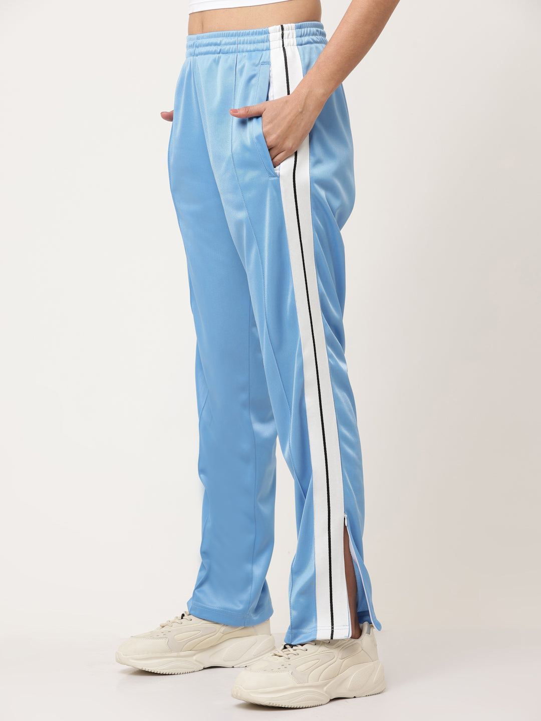 A pair of blue straight fit track pants with white side stripe detailing and a visible zipper at the bottom, held by a model.