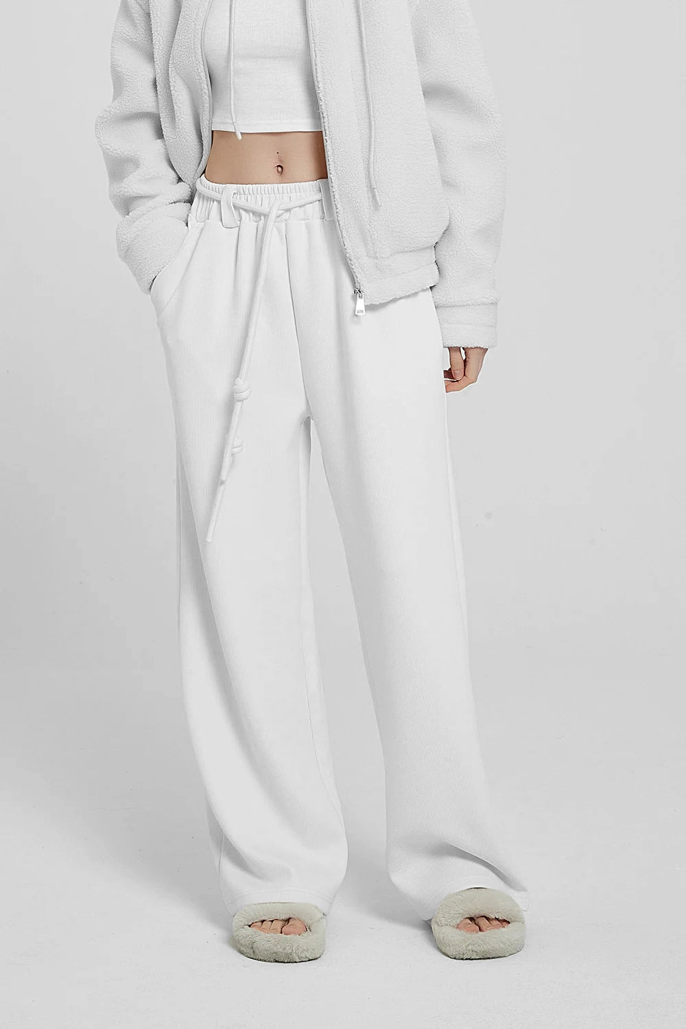 white high waist knitted pants and a white hoodie with a logo on the sleeve