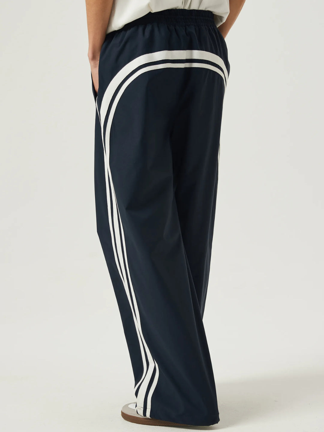 navy blue race track pants with white stripes on the side and an elasticated waistband with a drawstring