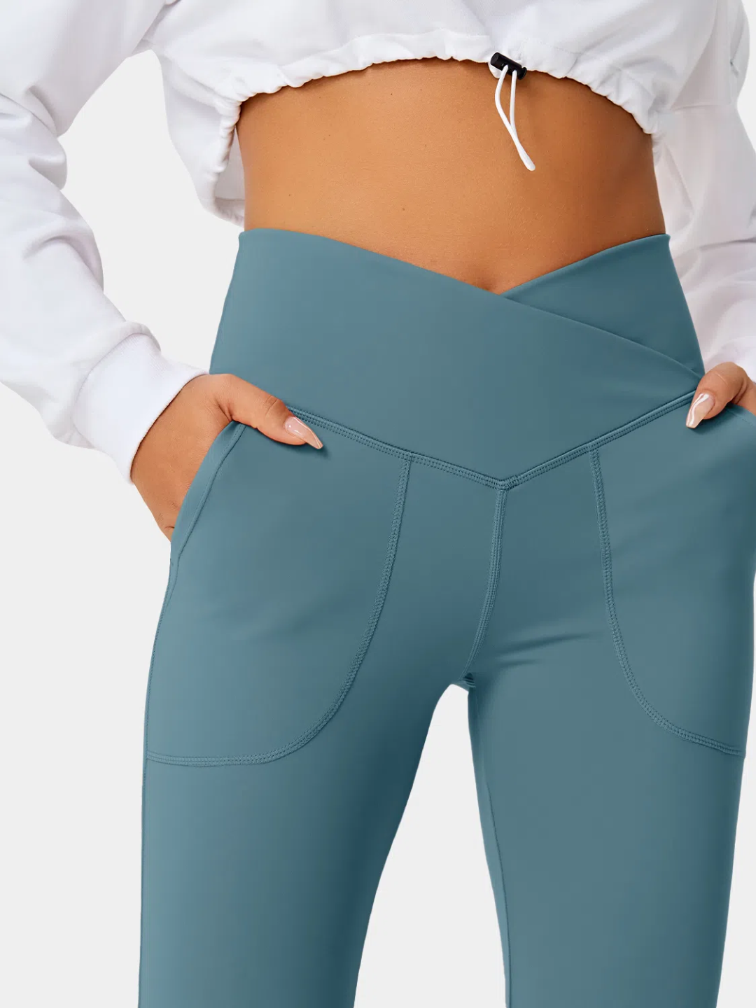 A person wearing teal flare leggings with a split hem, paired with a white cropped top and white sneakers.