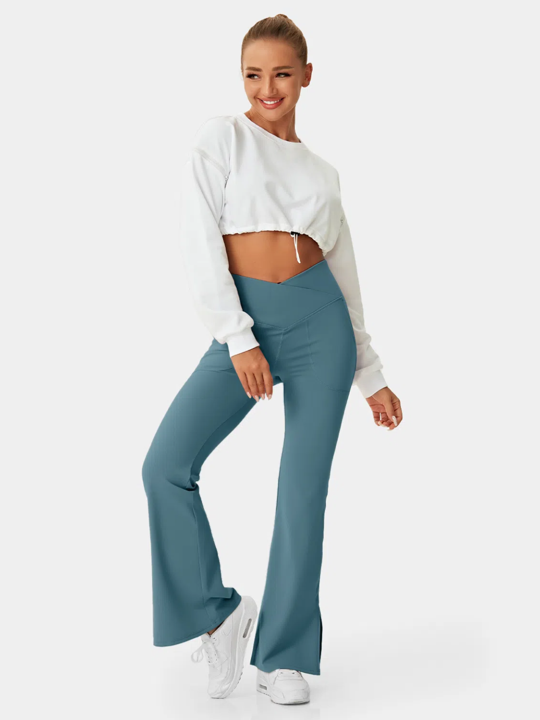 A person wearing teal flare leggings with a split hem, paired with a white cropped top and white sneakers.
