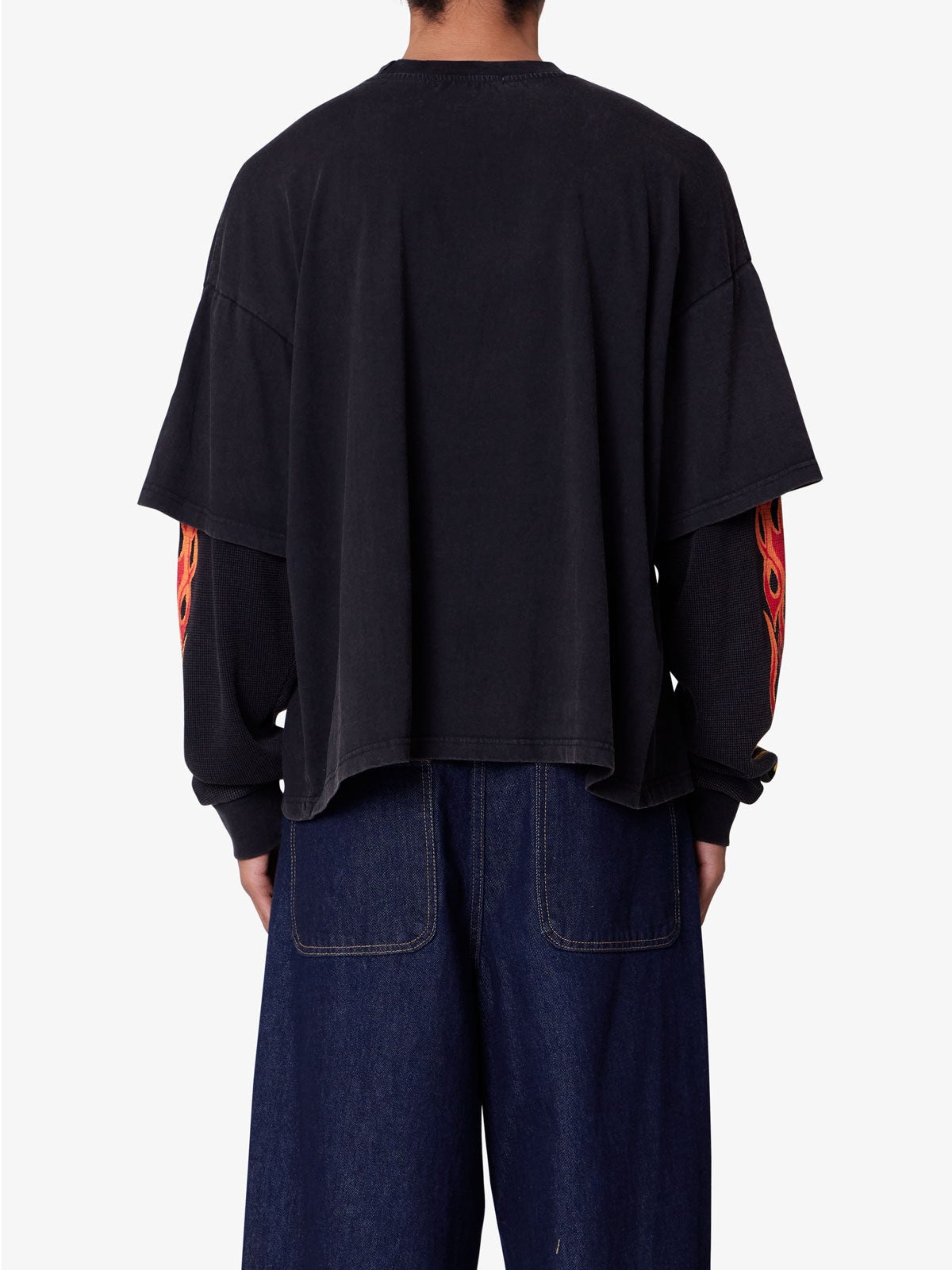 Person wearing a black oversized shirt with red designs on sleeves against a white background