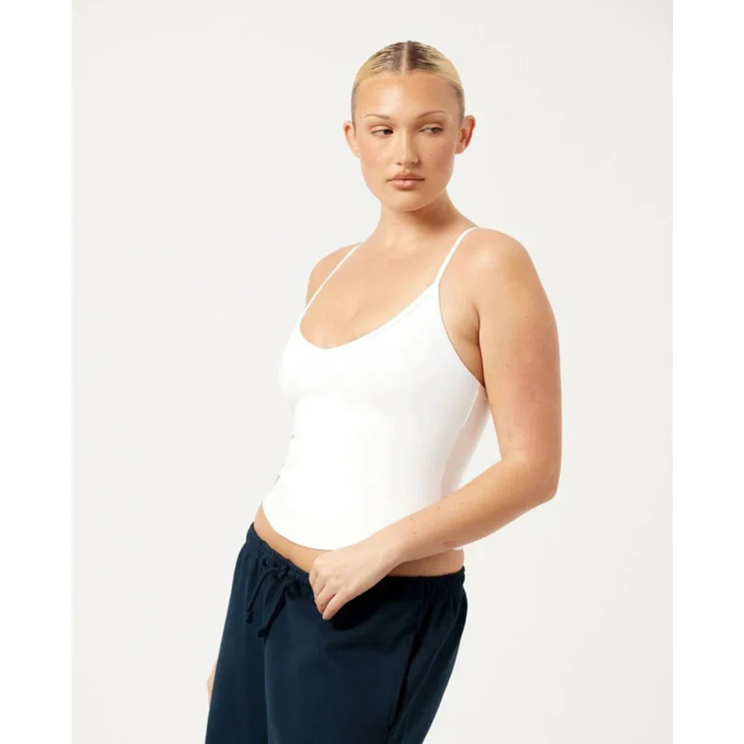 Woman wearing a white tank top and navy pants on a light gray background