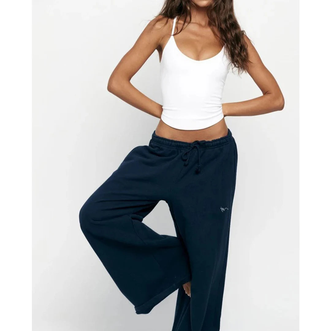 Woman wearing a white tank top and navy blue pants on a white background