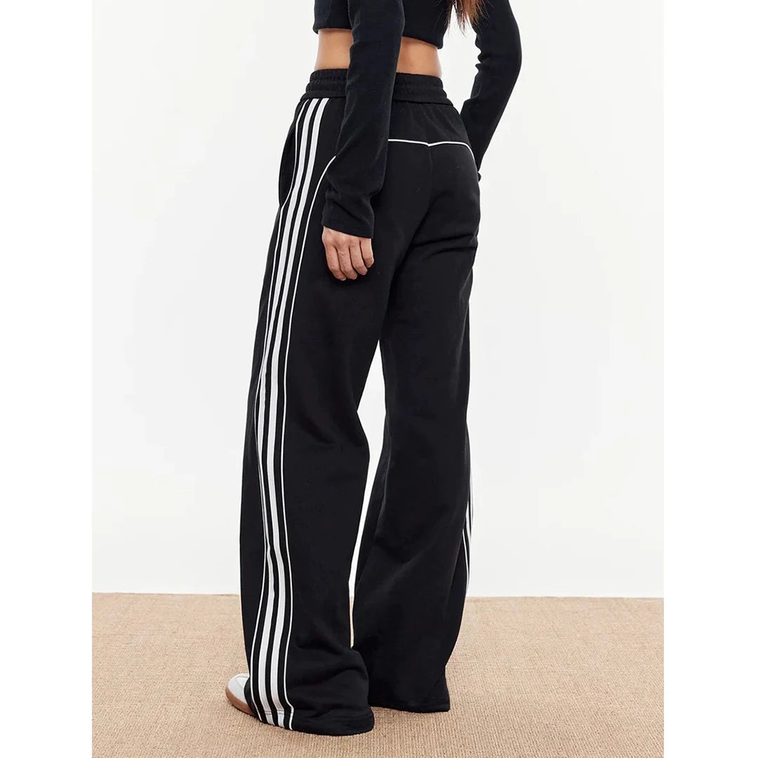 Black track pants with white stripes worn by a person on a plain background