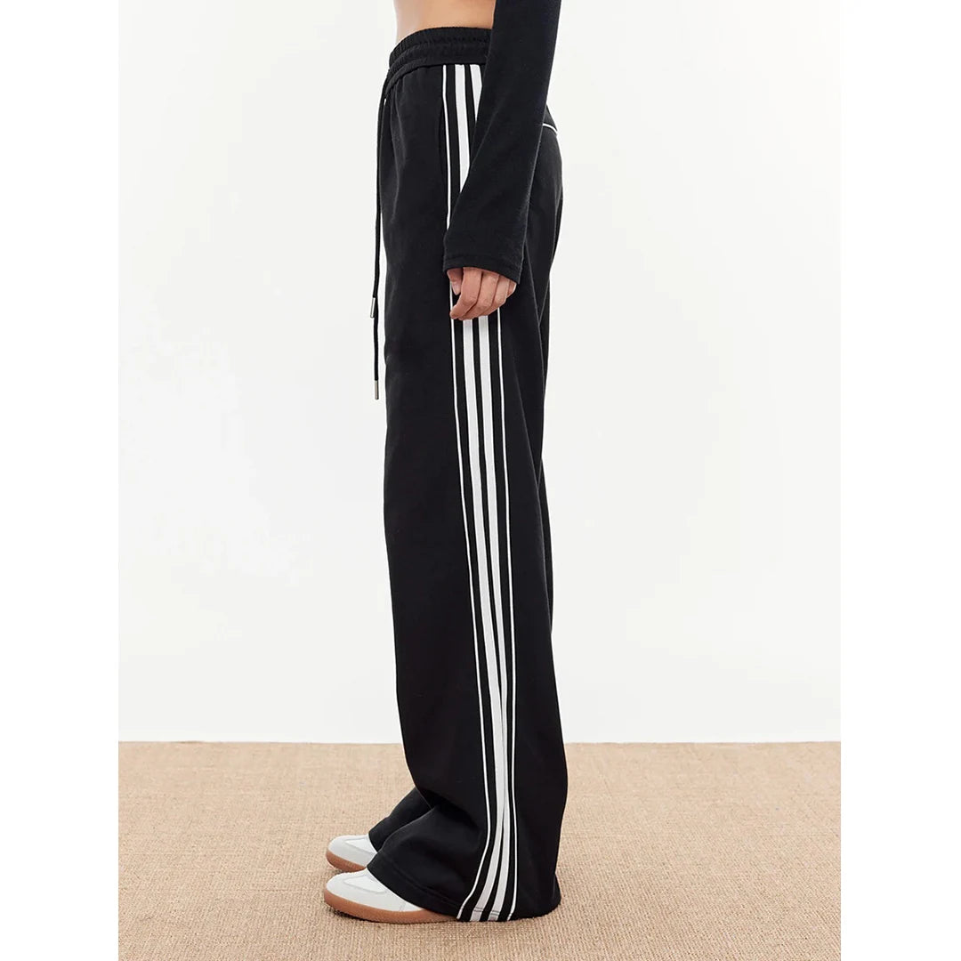 Black track pants with white stripes worn by a person on a beige floor.