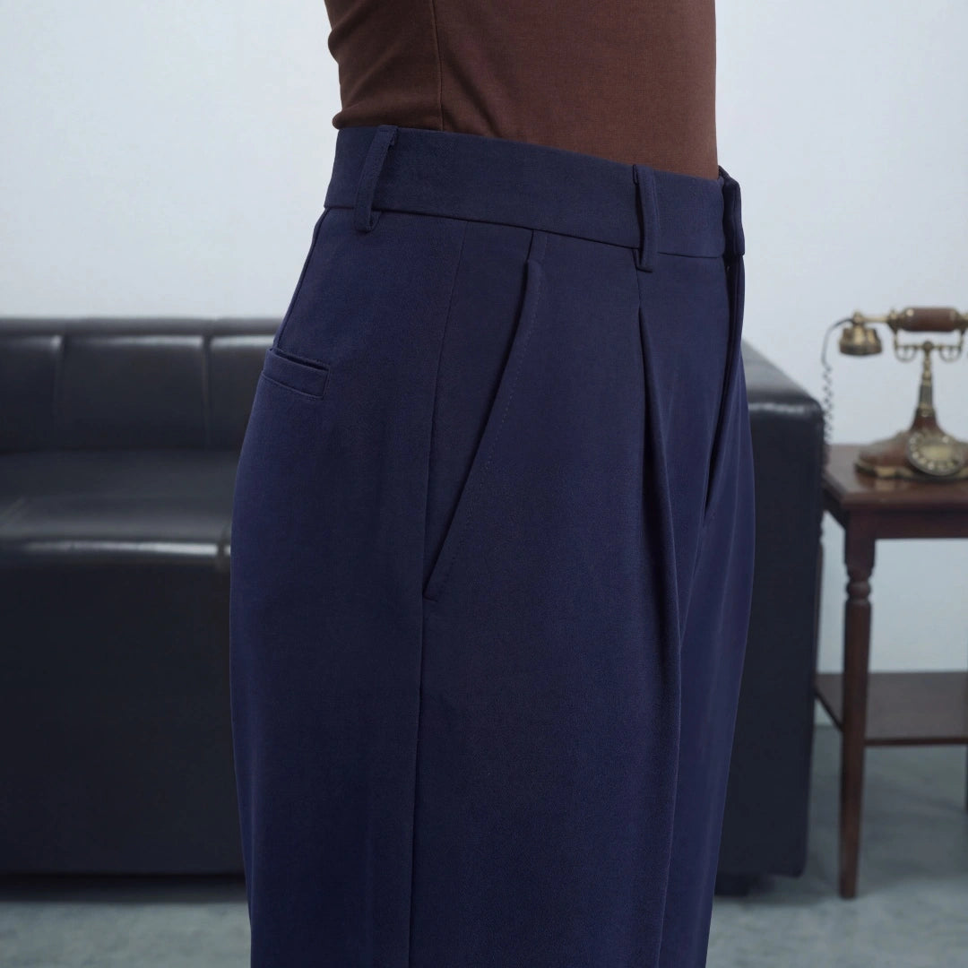 Navy pleated pants worn by a person in an indoor setting with a couch and table in the background.
