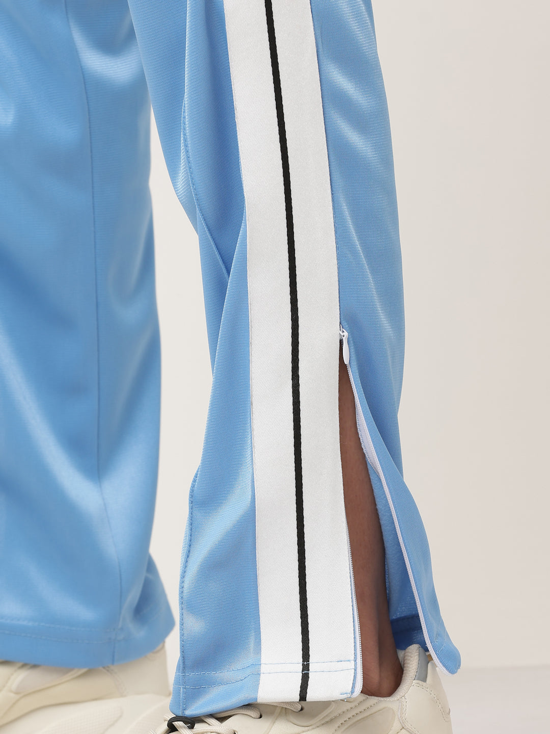 A pair of blue straight fit track pants with white side stripe detailing and a visible zipper at the bottom, held by a model.