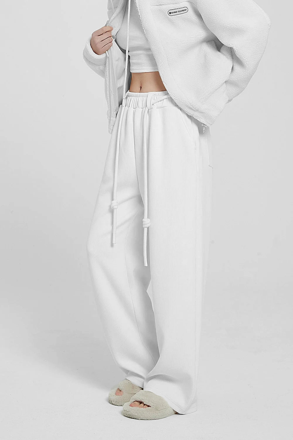 white high waist knitted pants and a white hoodie with a logo on the sleeve