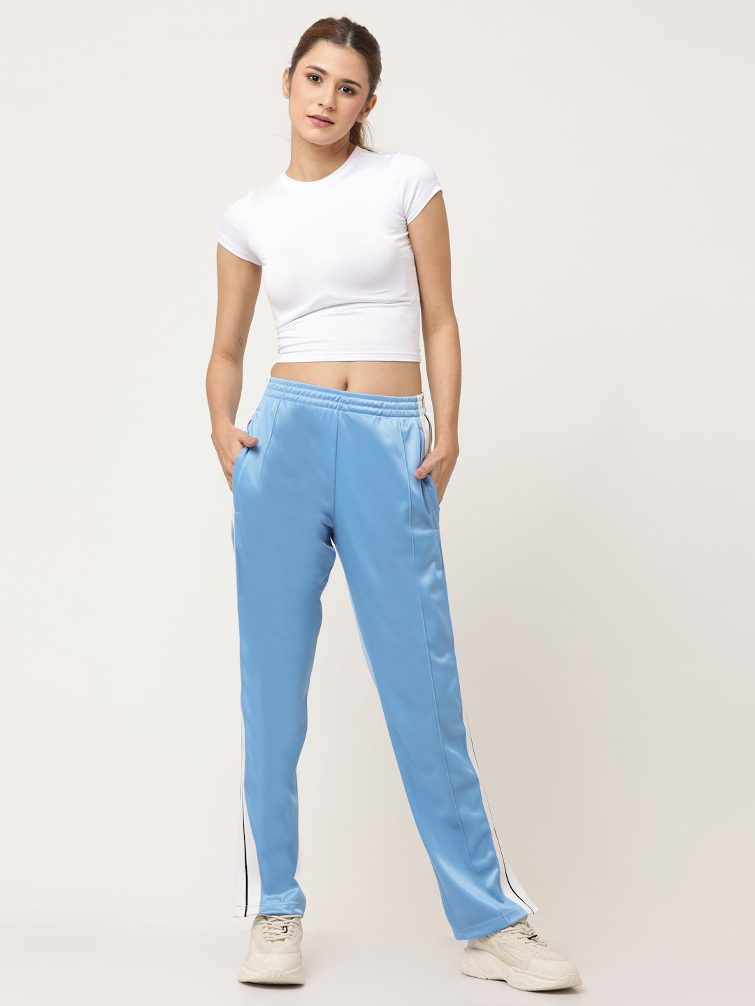 A pair of blue straight fit track pants with white side stripe detailing and a visible zipper at the bottom, held by a model.