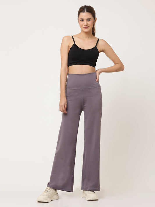 A woman standing and posing in lavender high-waisted full-length yoga pants with a solid black sports top.