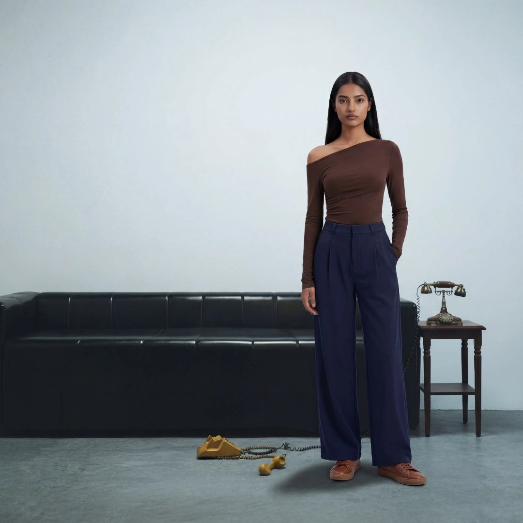 Woman in brown top and blue pants standing in a minimalistic room with a black sofa and small table.