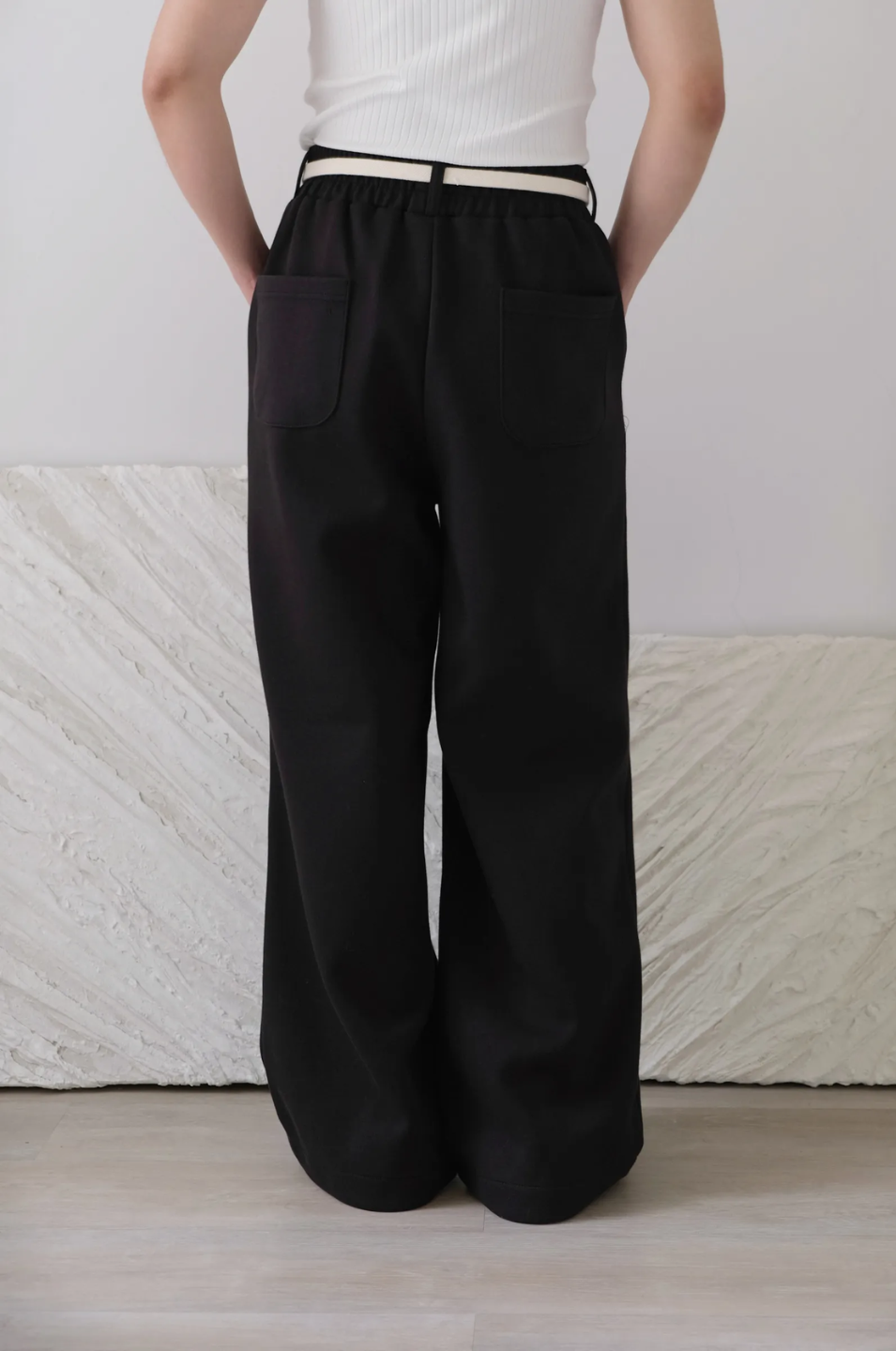 Person wearing black wide-leg pants and a white top against a light background
