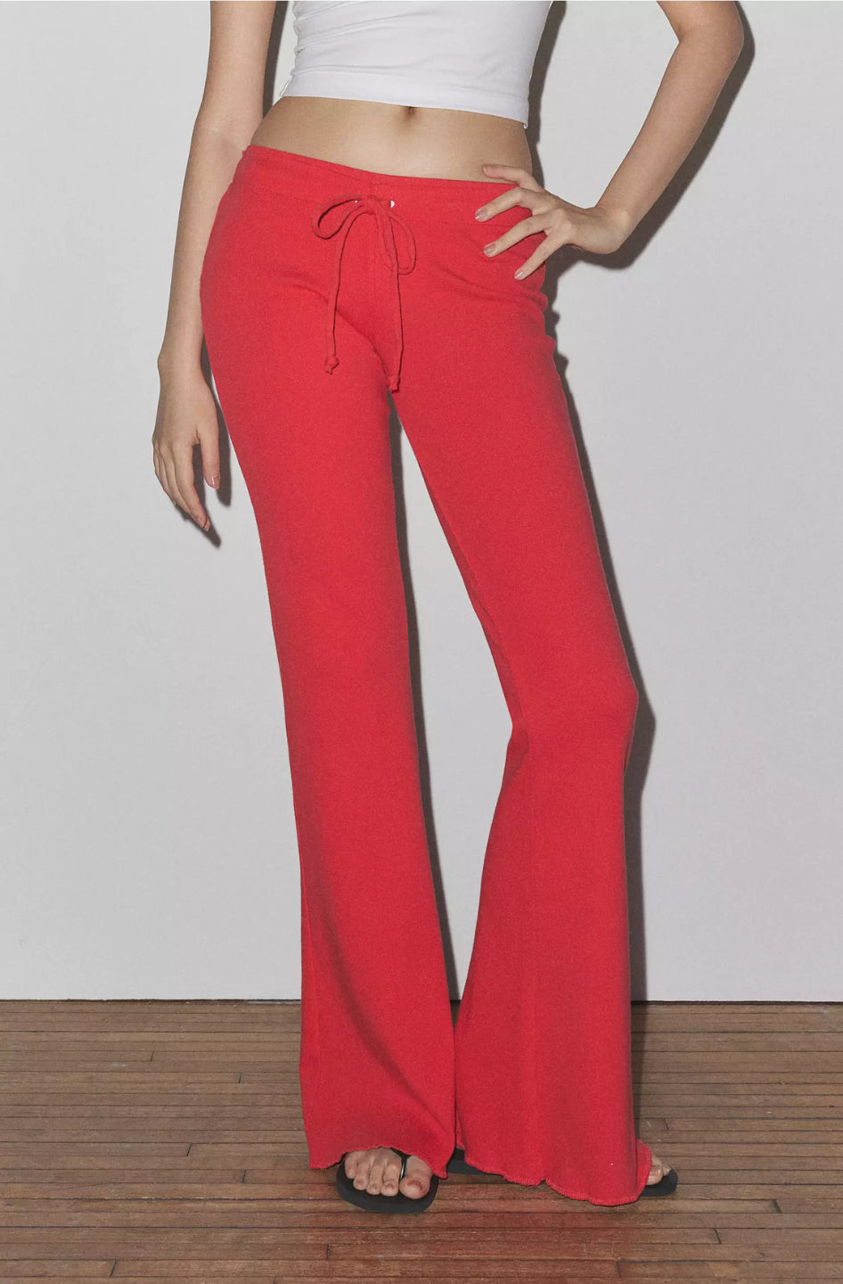 A person standing wearing red low-rise flared sweatpants with an elasticized waistband and drawstrings.