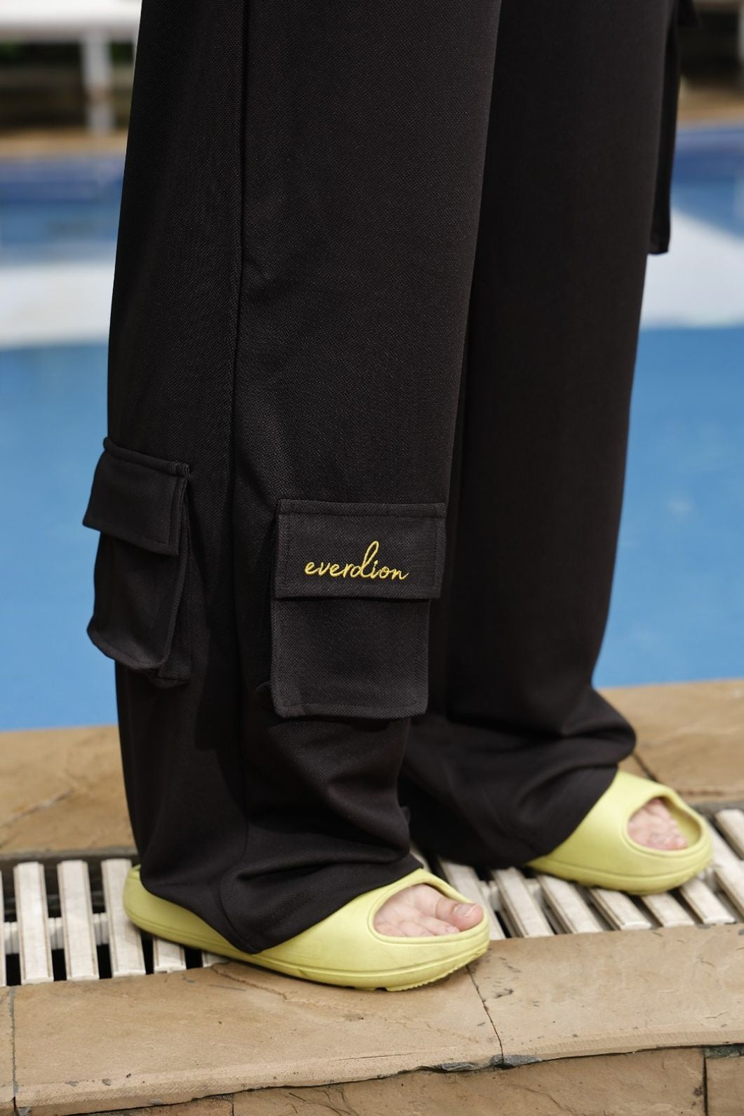 Person wearing black cargo pants with 'everdion' branding, standing on a wooden platform.