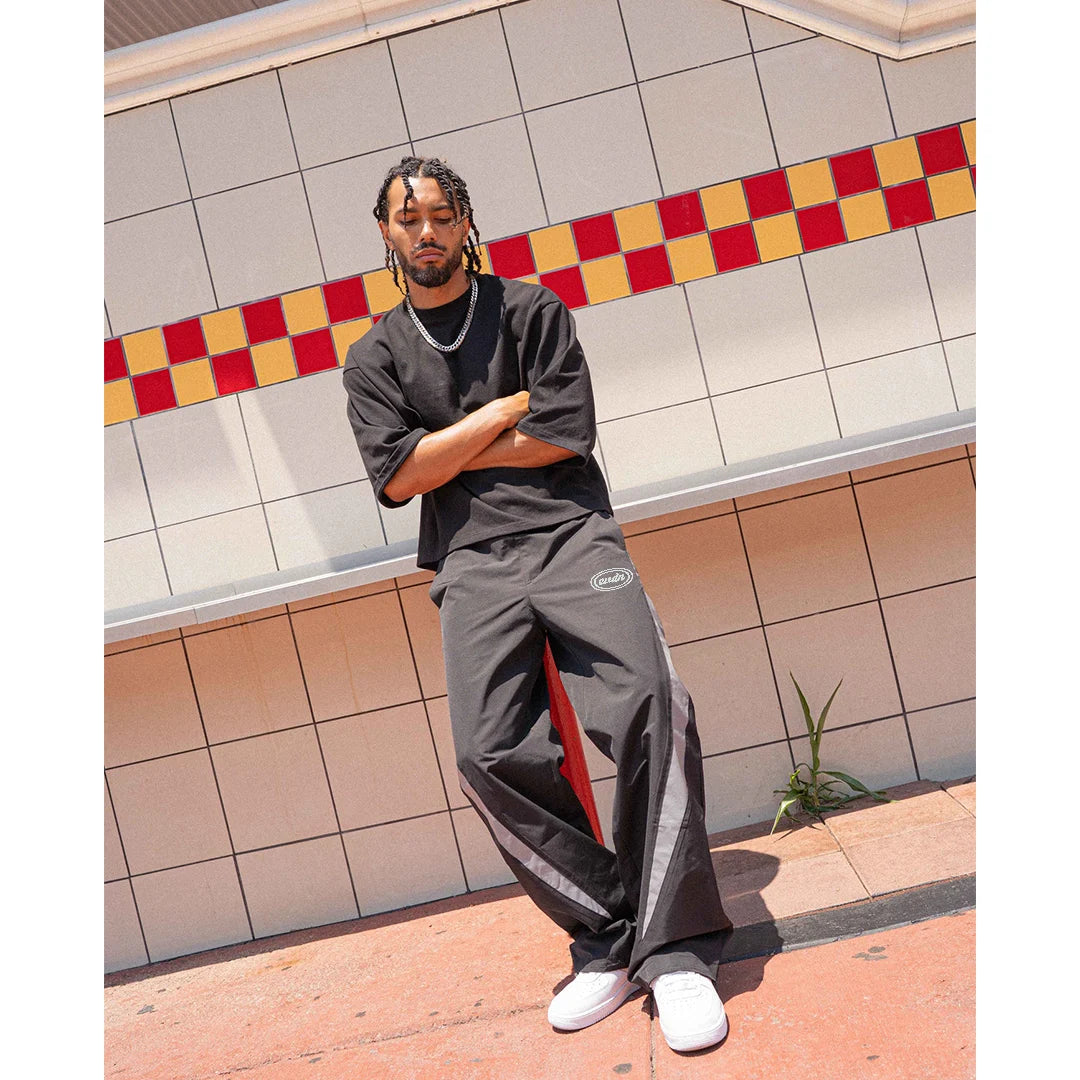 Person wearing a black outfit with red accents against a tiled wall.