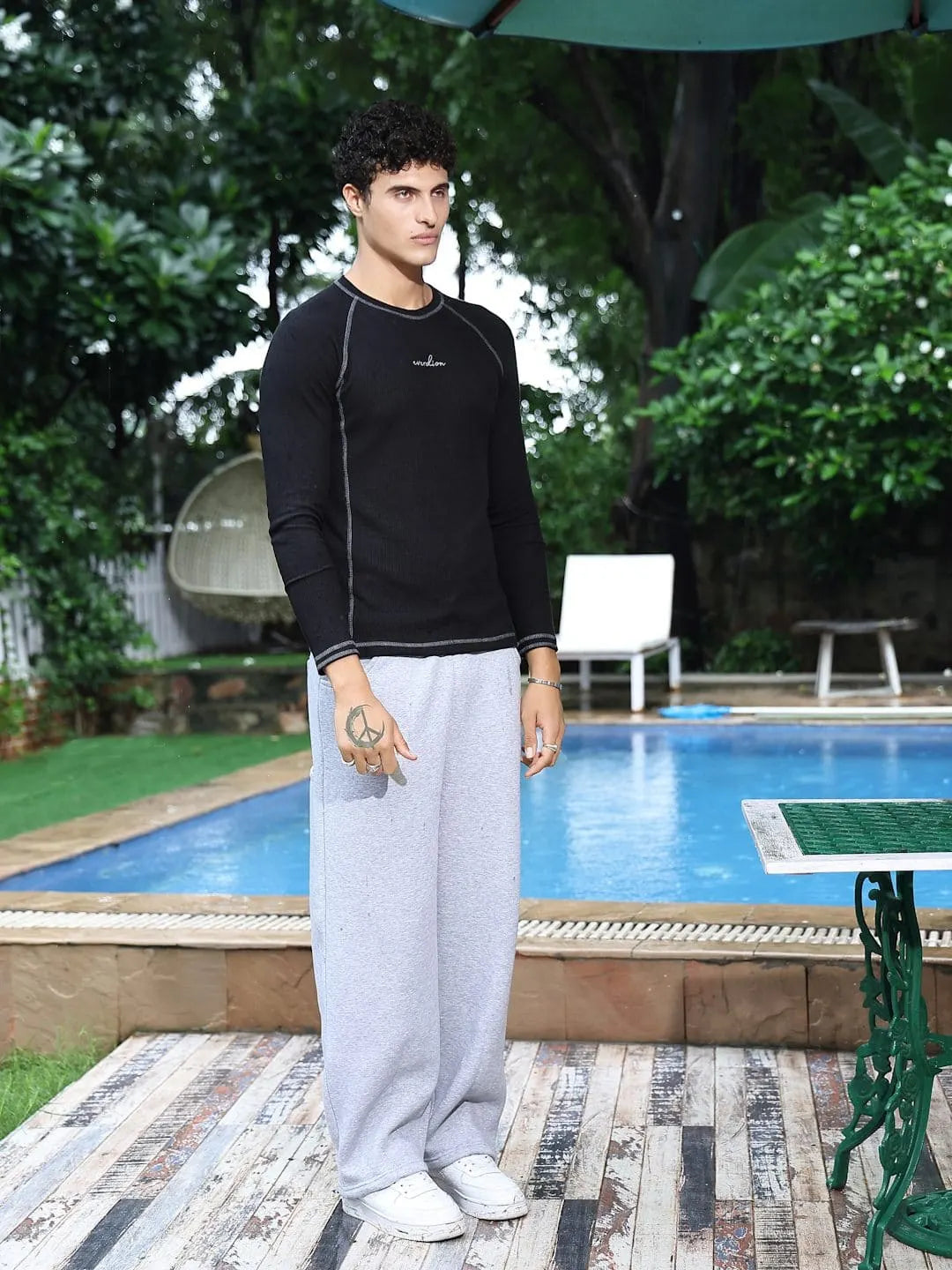 Man standing by a poolside wearing a black long-sleeve shirt and light gray pants.