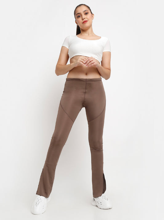 A woman standing, wearing brown side slit flare pants and a white cropped top.