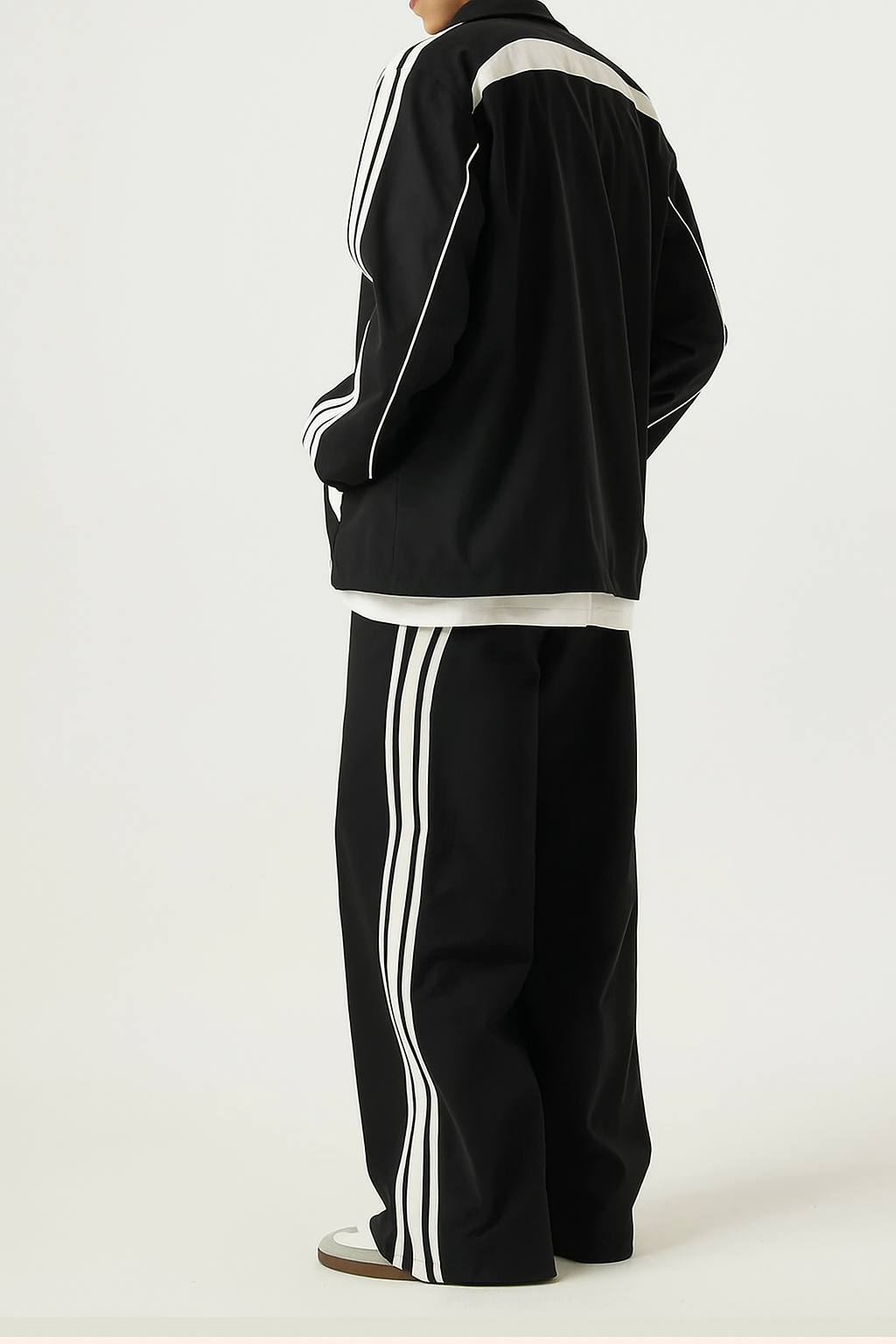 A person wearing a black tracksuit with white stripes on a white background