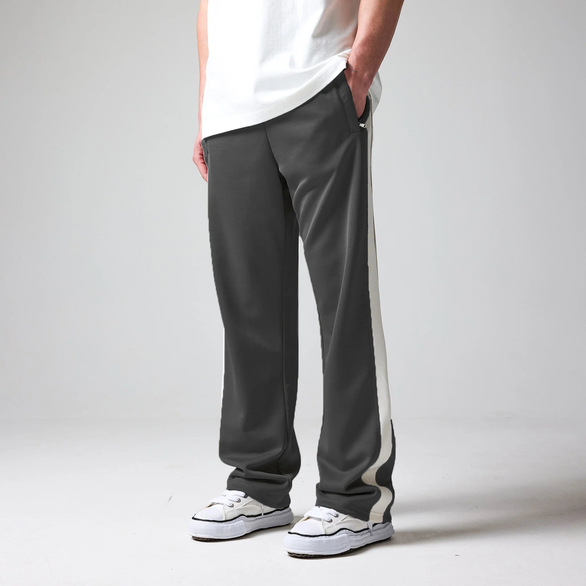 Person wearing grey track pants with a white stripe on a plain background