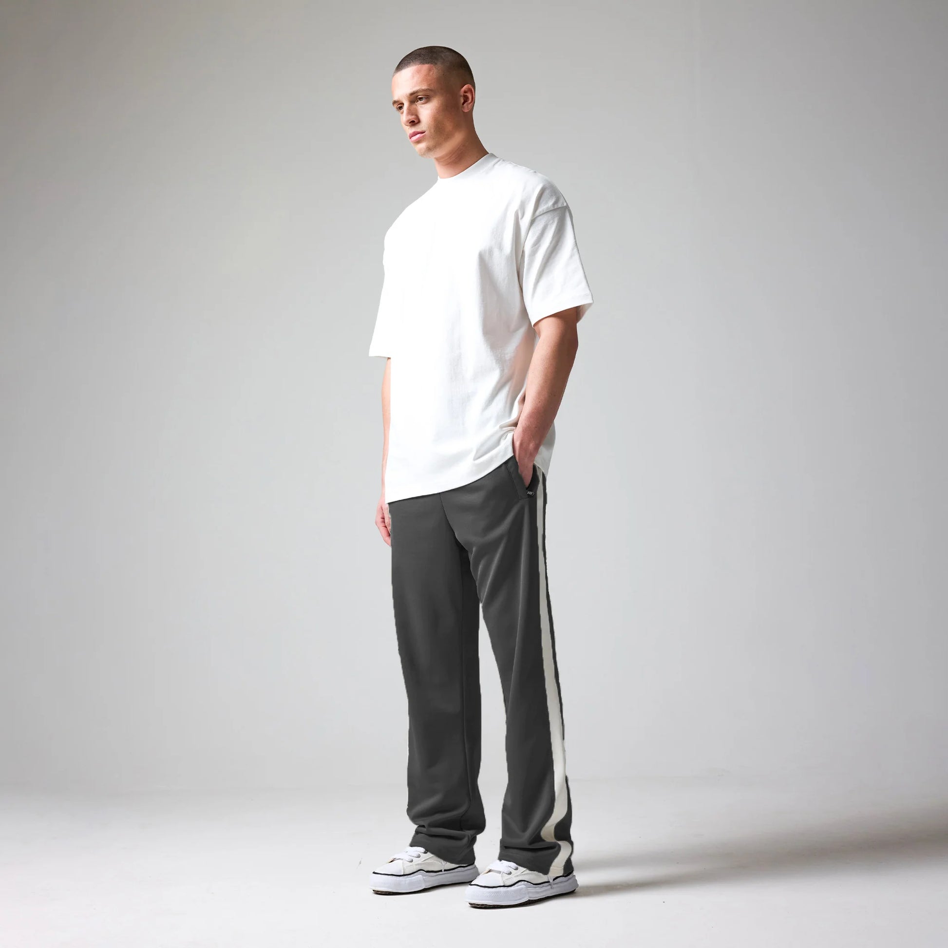 Man wearing a white t-shirt and gray pants with a stripe, standing against a plain background