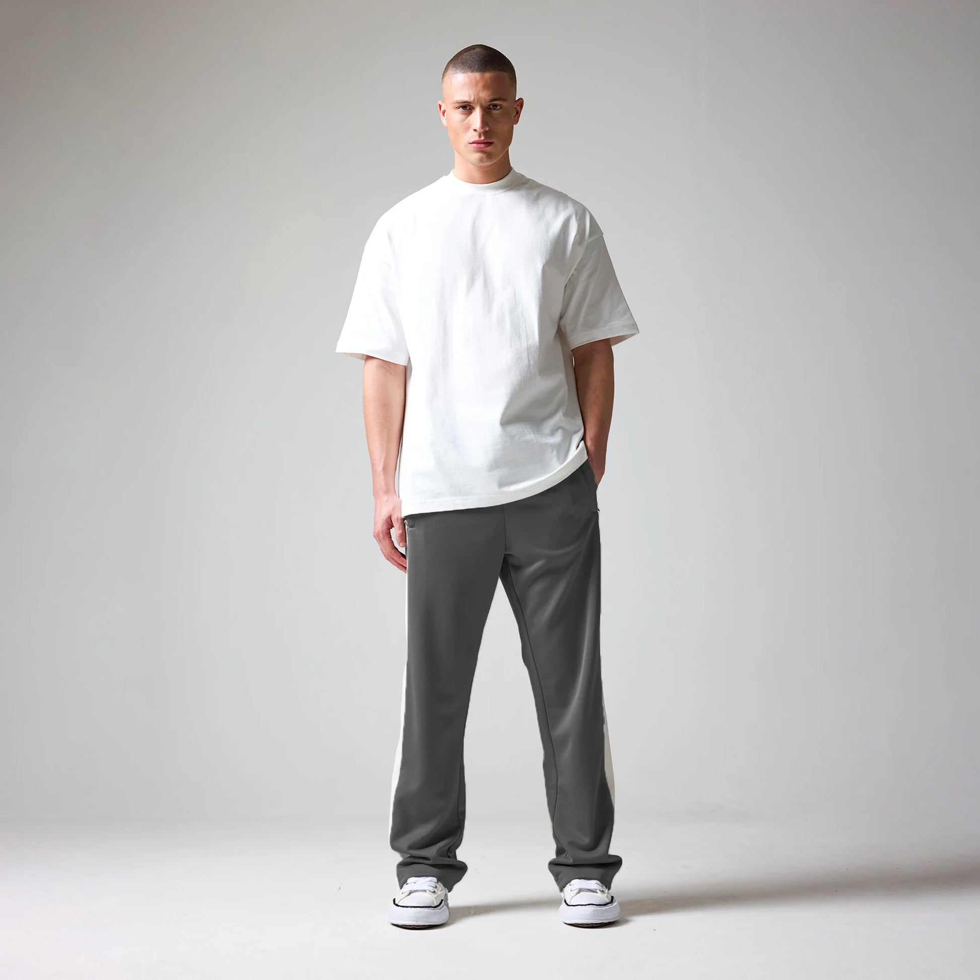 A man wearing a white t-shirt and grey pants on a plain background
