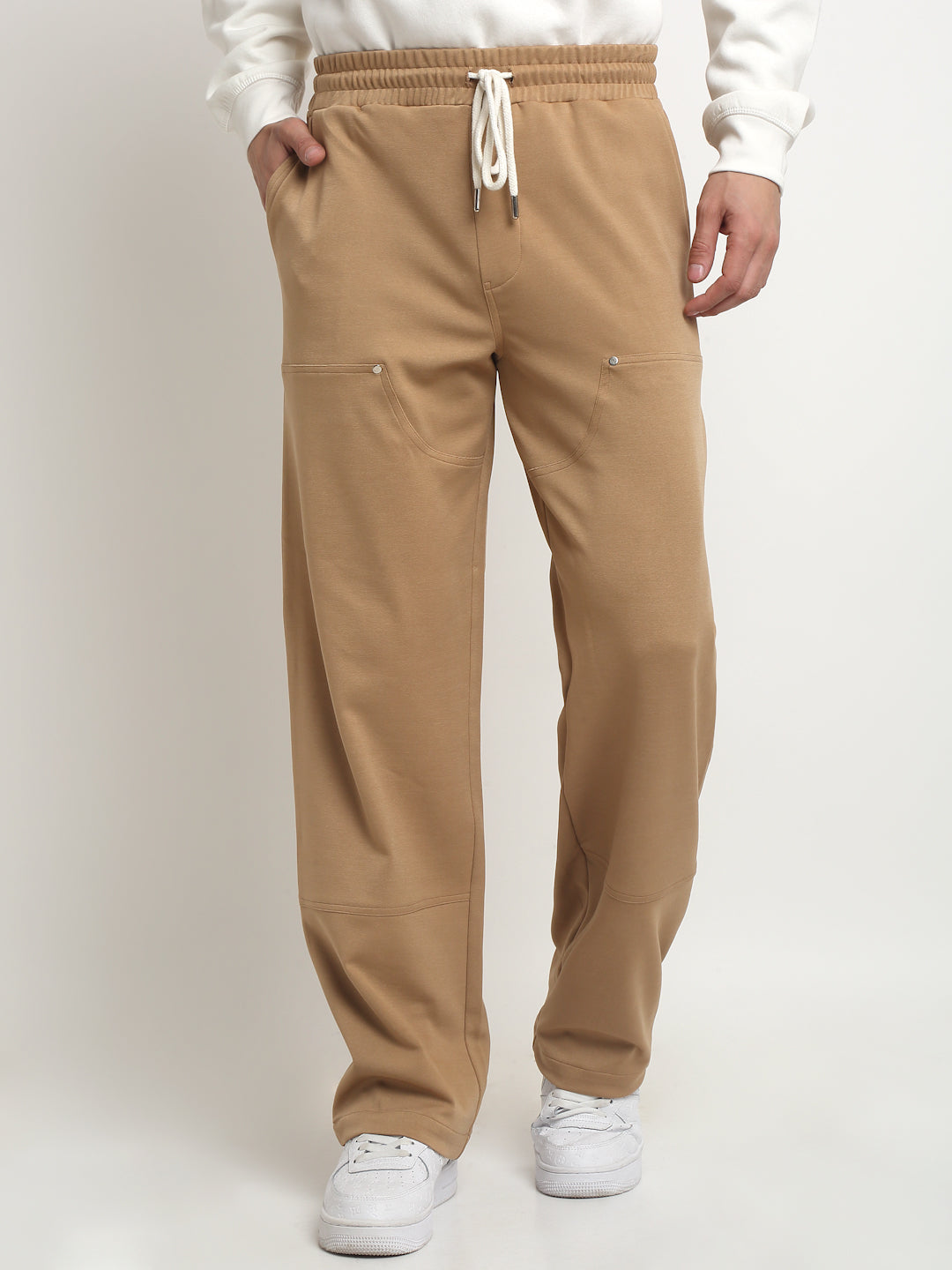 A model wearing camel brown straight-fit trousers with rivets and a drawstring waistband.