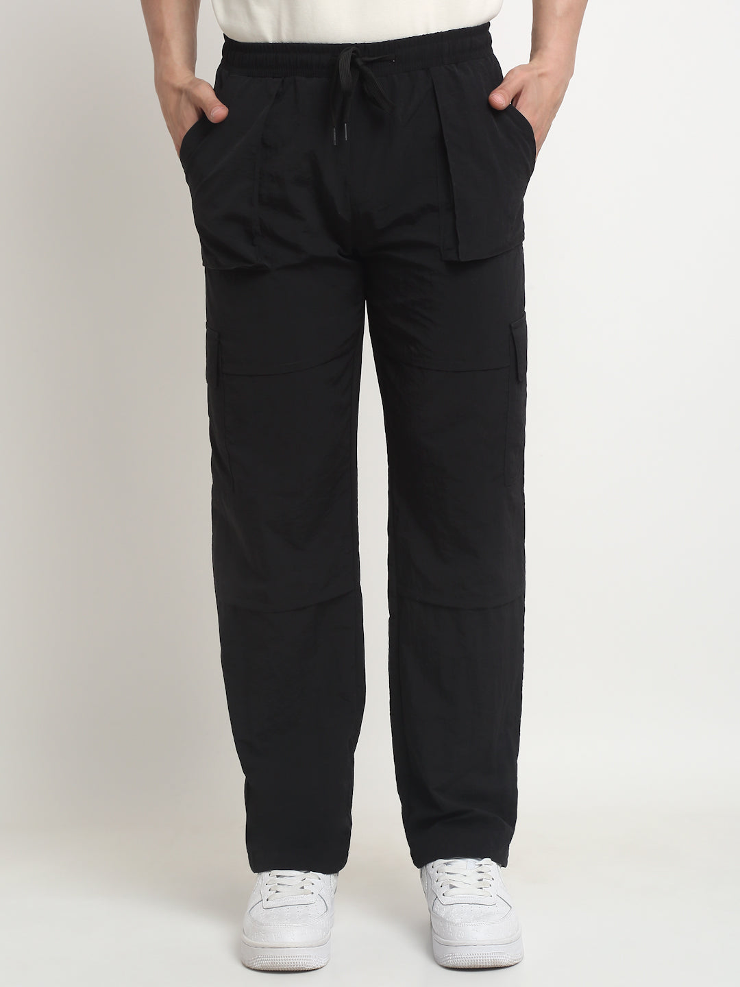 A person standing with hands in pockets, wearing black technical carpenter cargo pants and white sneakers.
