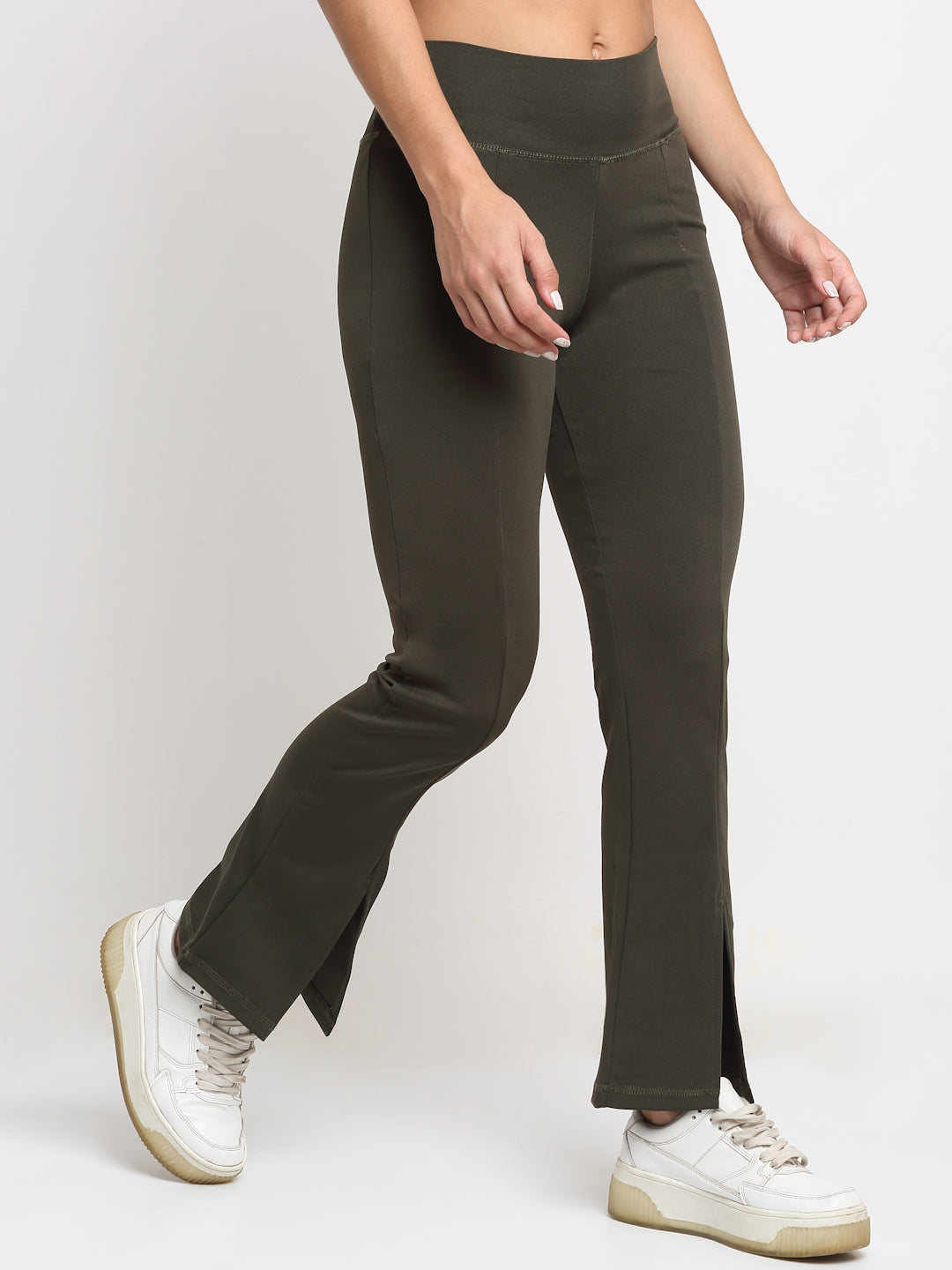 A pair of high waist green yoga pants with front slits and a flared leg design, being modeled by a person wearing white sneakers.