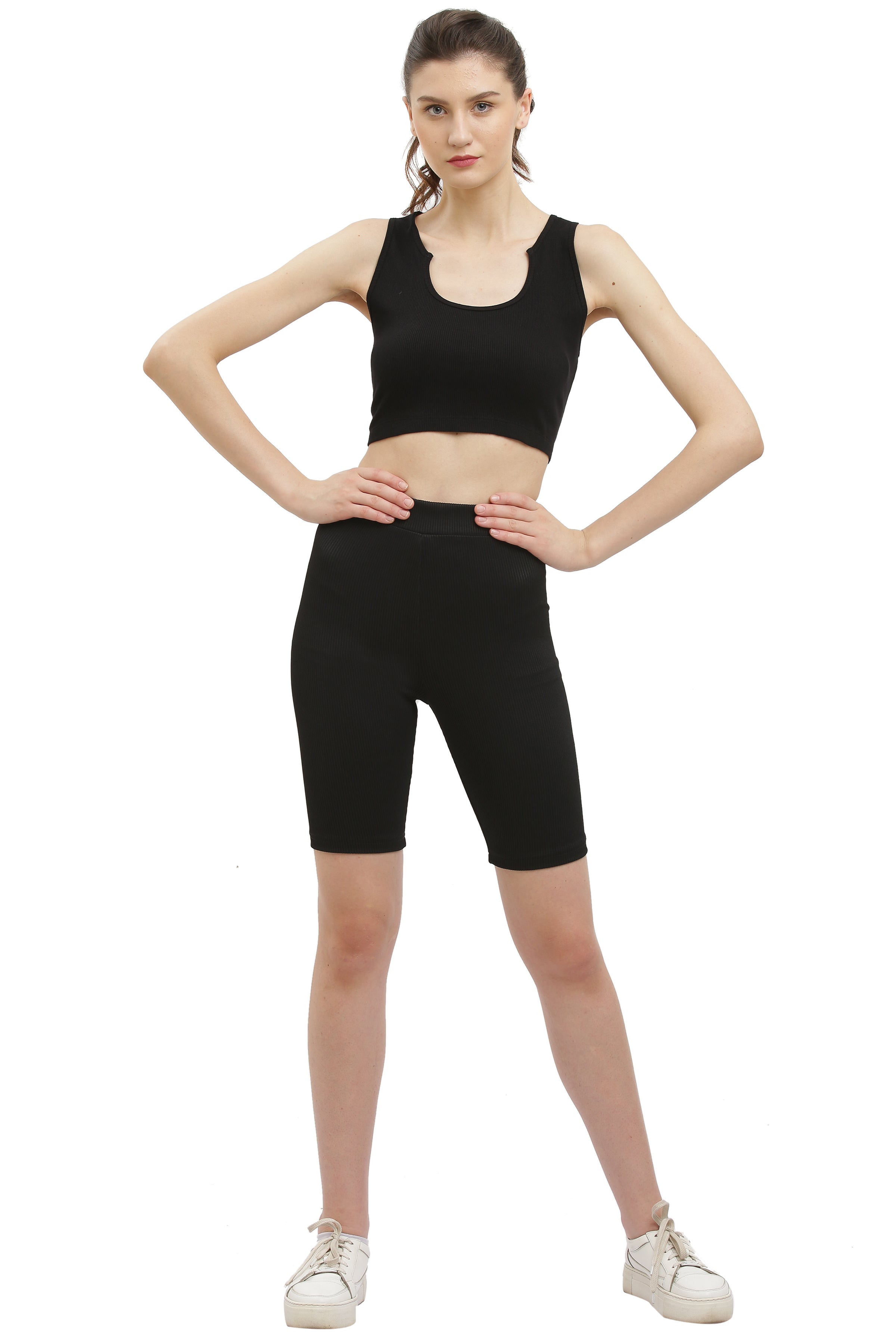 A woman wearing a black rib sleeveless crop top and black pants.