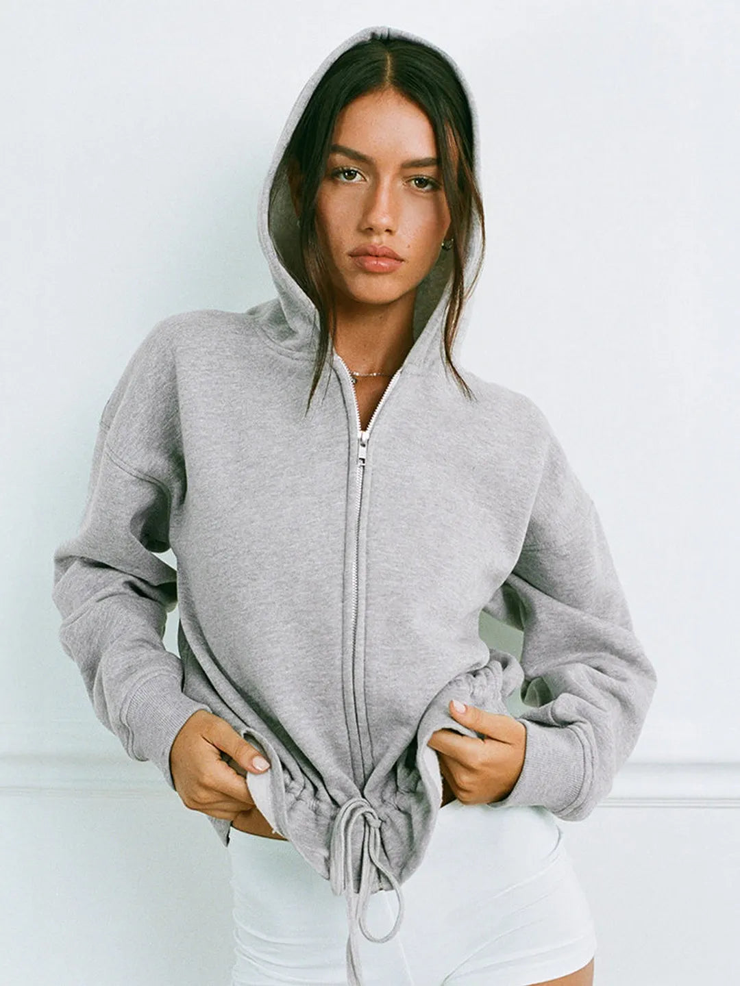 Woman wearing a gray zip-up hoodie against a light background