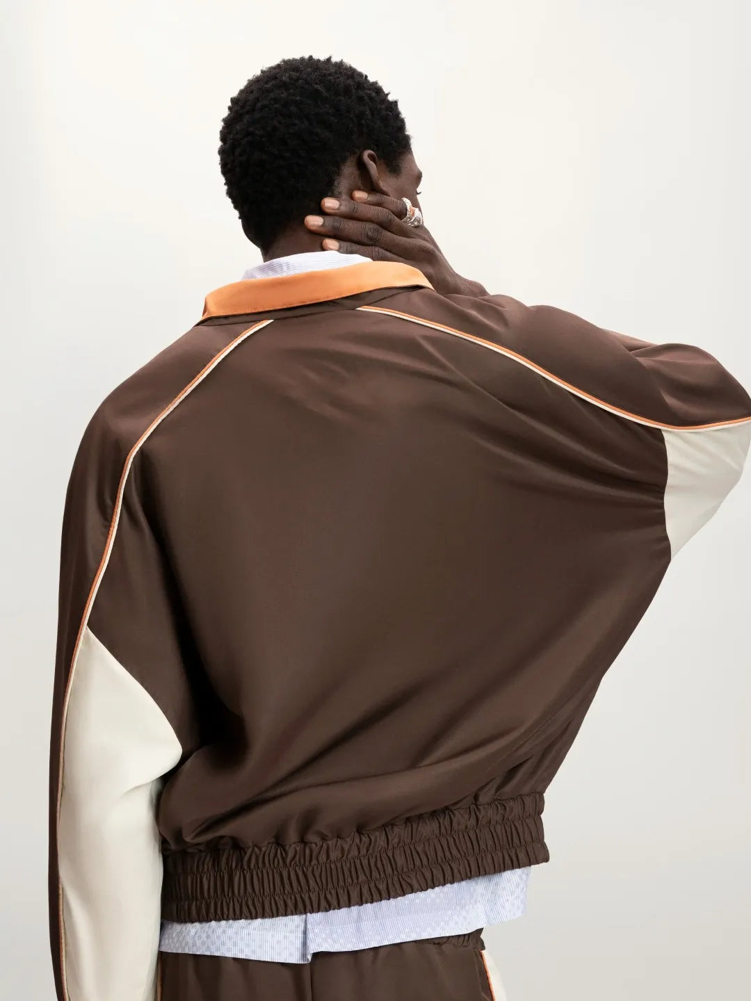 Person wearing a brown jacket with a white shirt underneath on a plain background