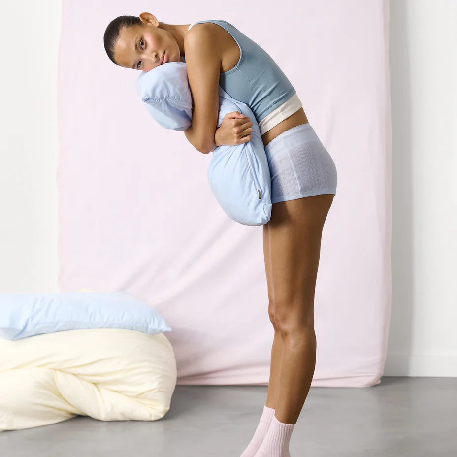 Woman embracing a large pillow with a neutral background