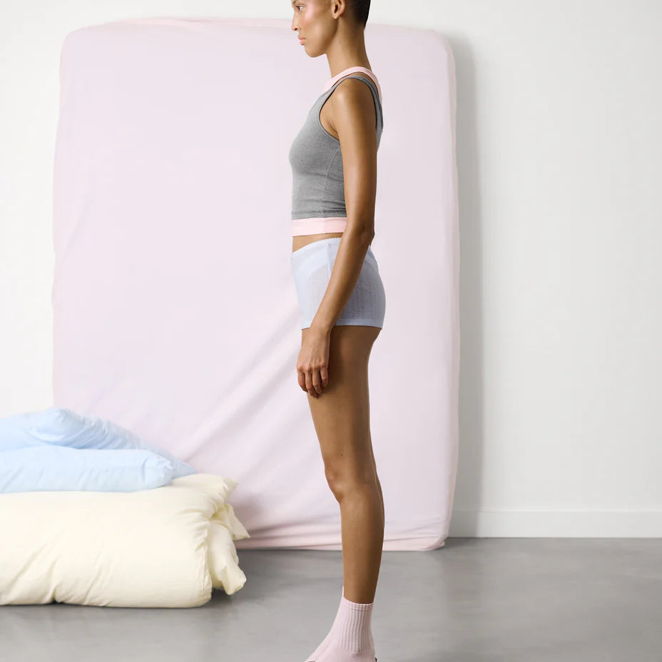 Woman standing next to a mattress with colorful pillows on a plain background