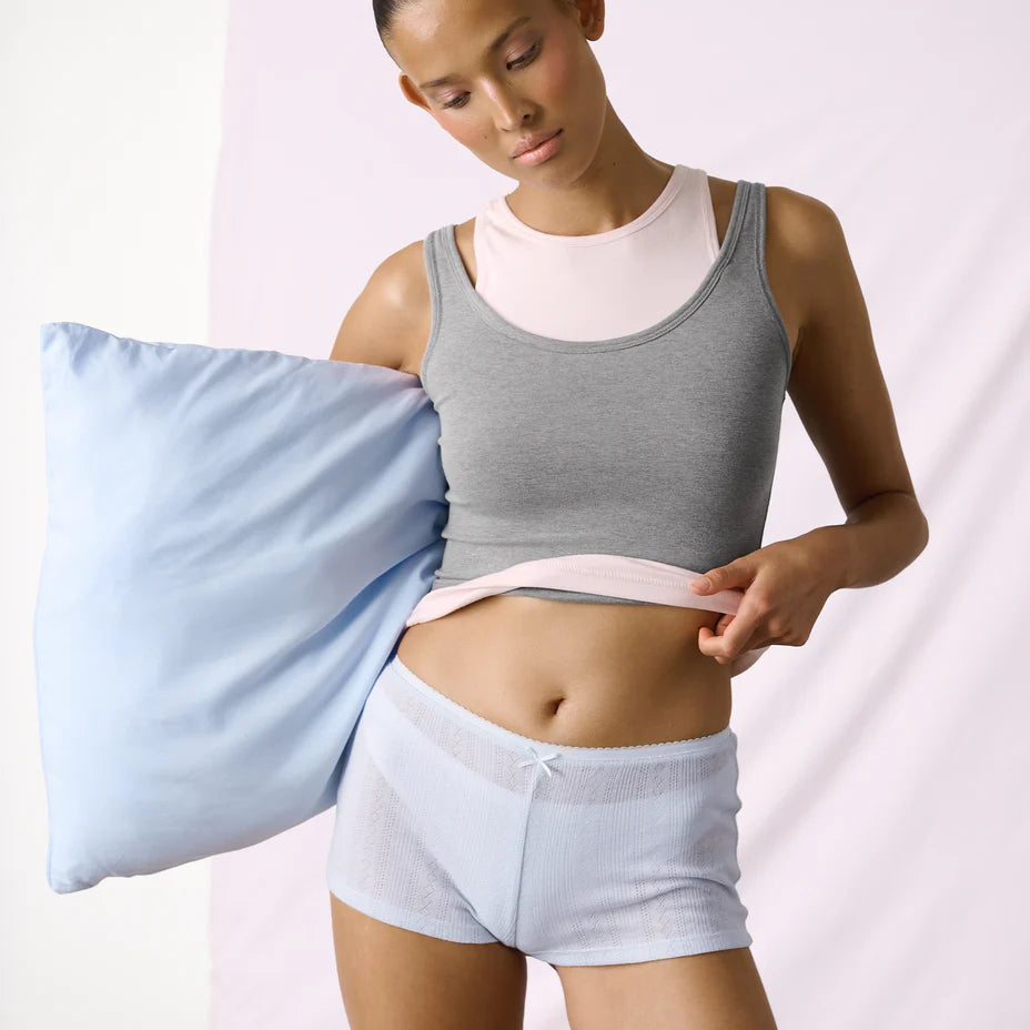 Woman holding a blue satin pillowcase against a white background