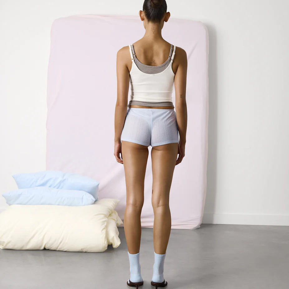 Woman standing in front of a bed with pillows and blankets.