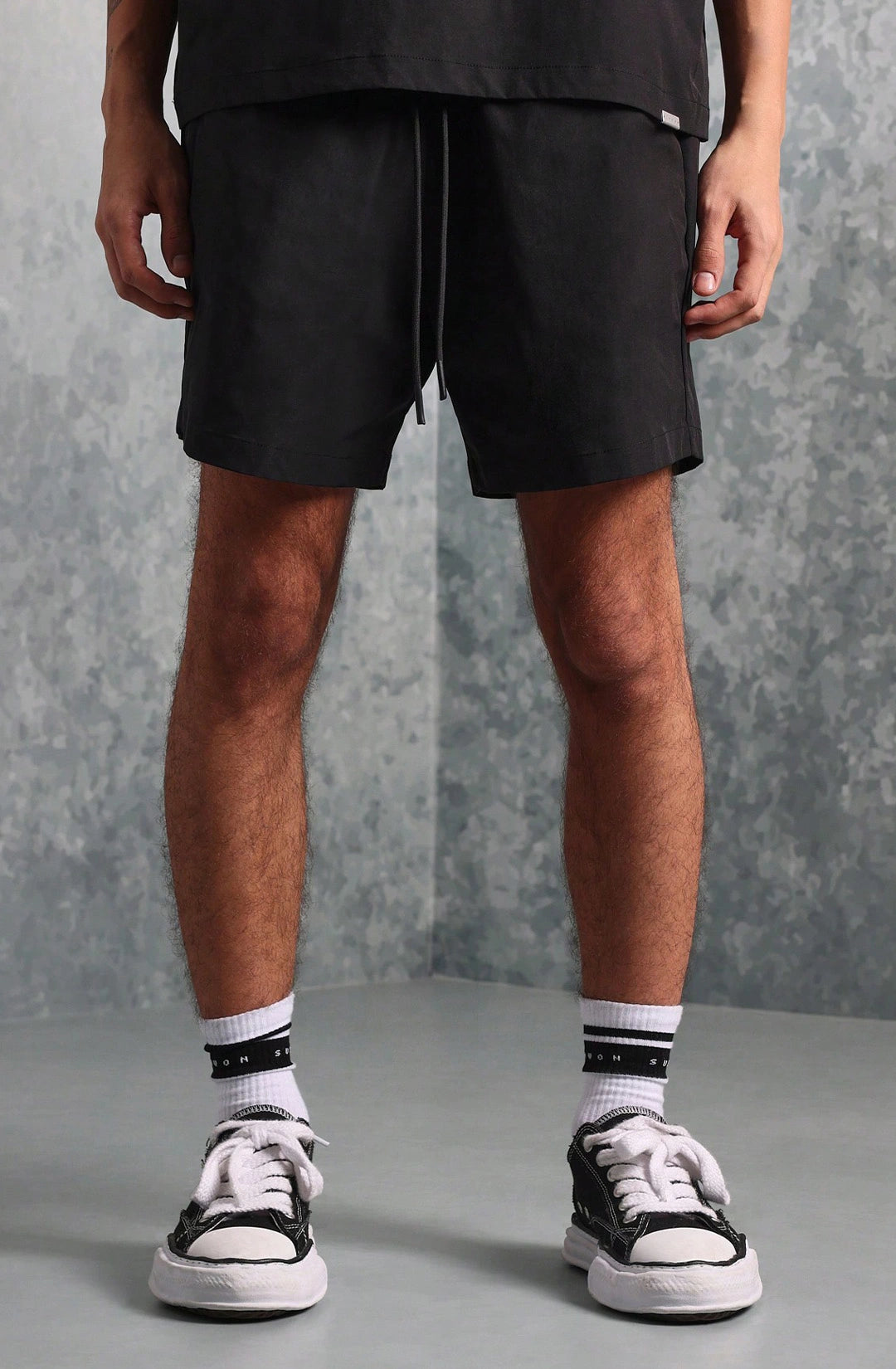 Person wearing black shorts and black and white sneakers on a gray background