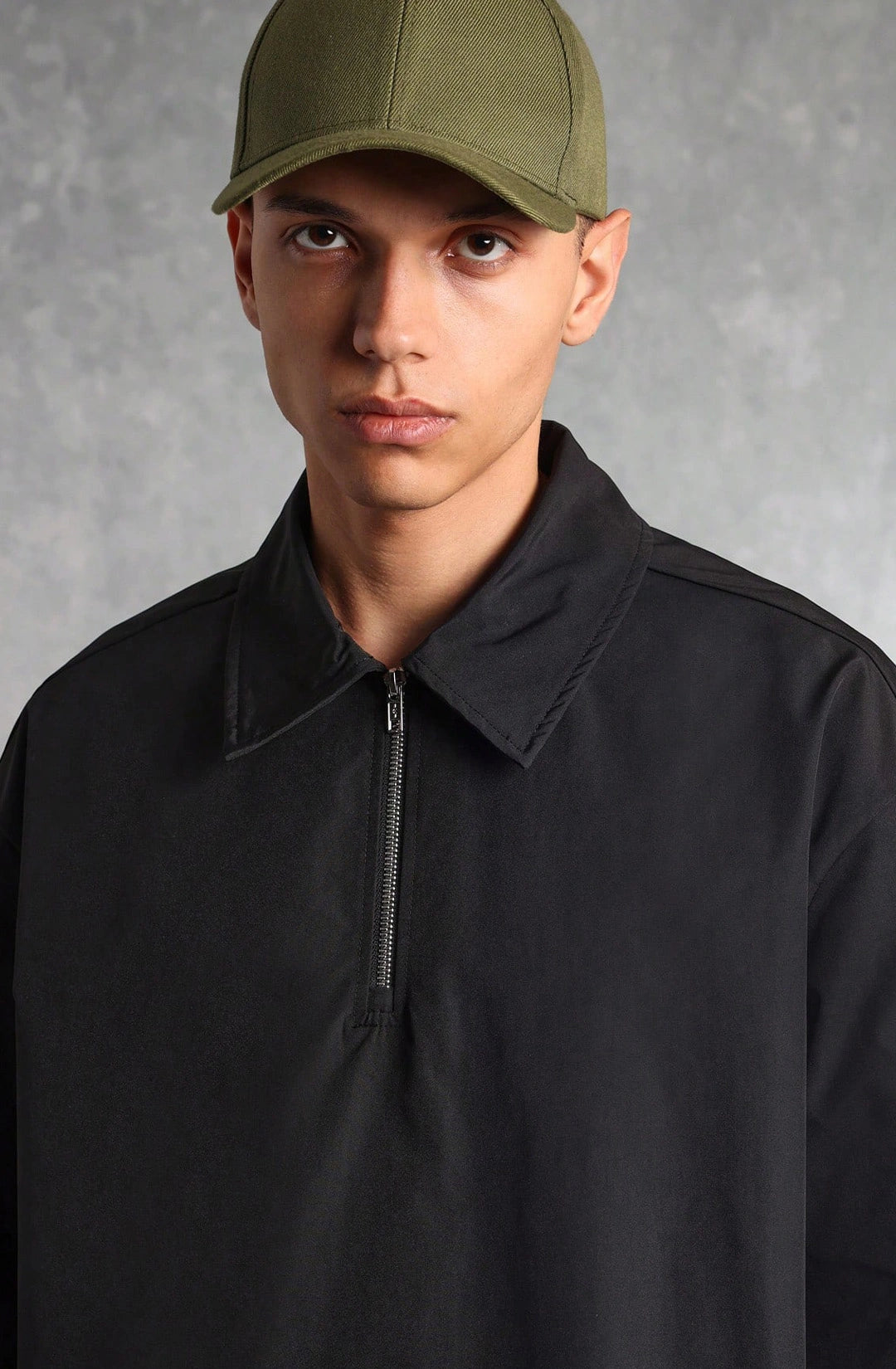 Person wearing a black jacket and green cap against a gray background